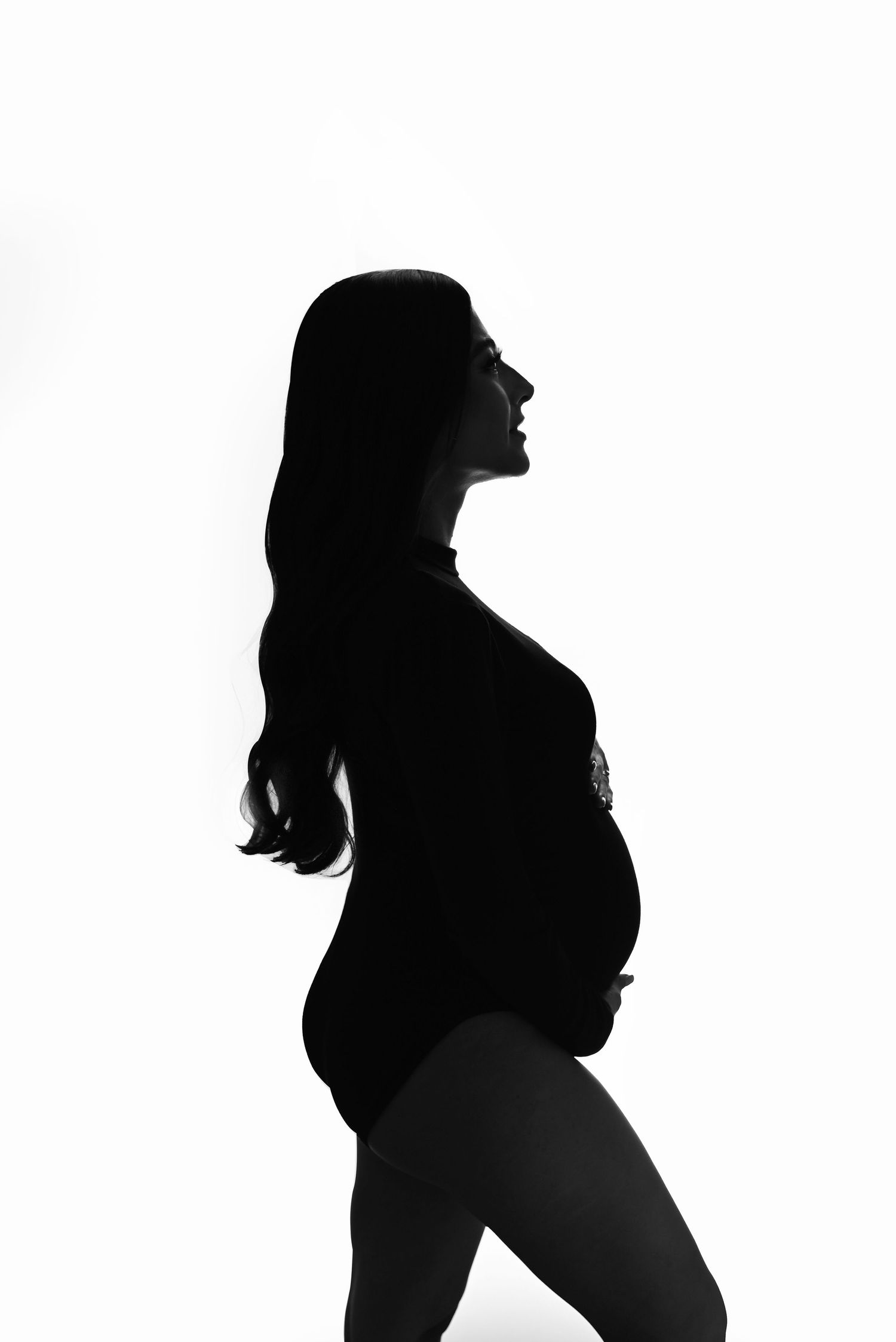 Dramatic silhouette of an expectant mother against white background.