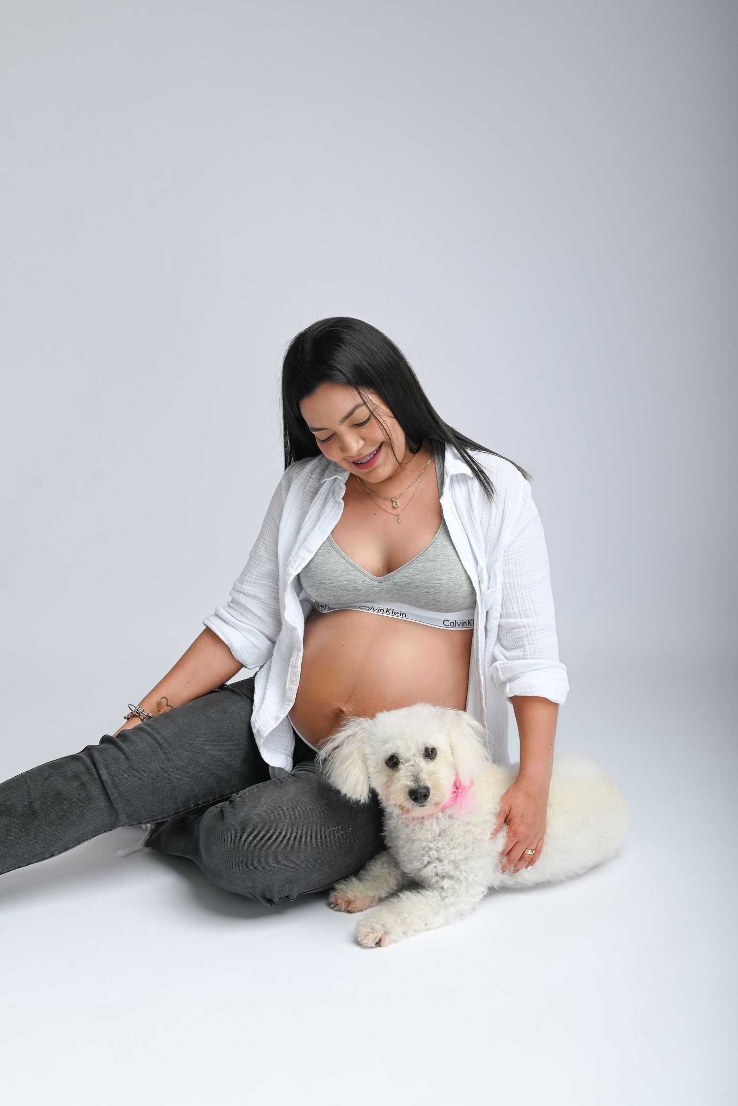 A relaxed lifestyle portrait with a white fluffy dog on a light gray studio background.