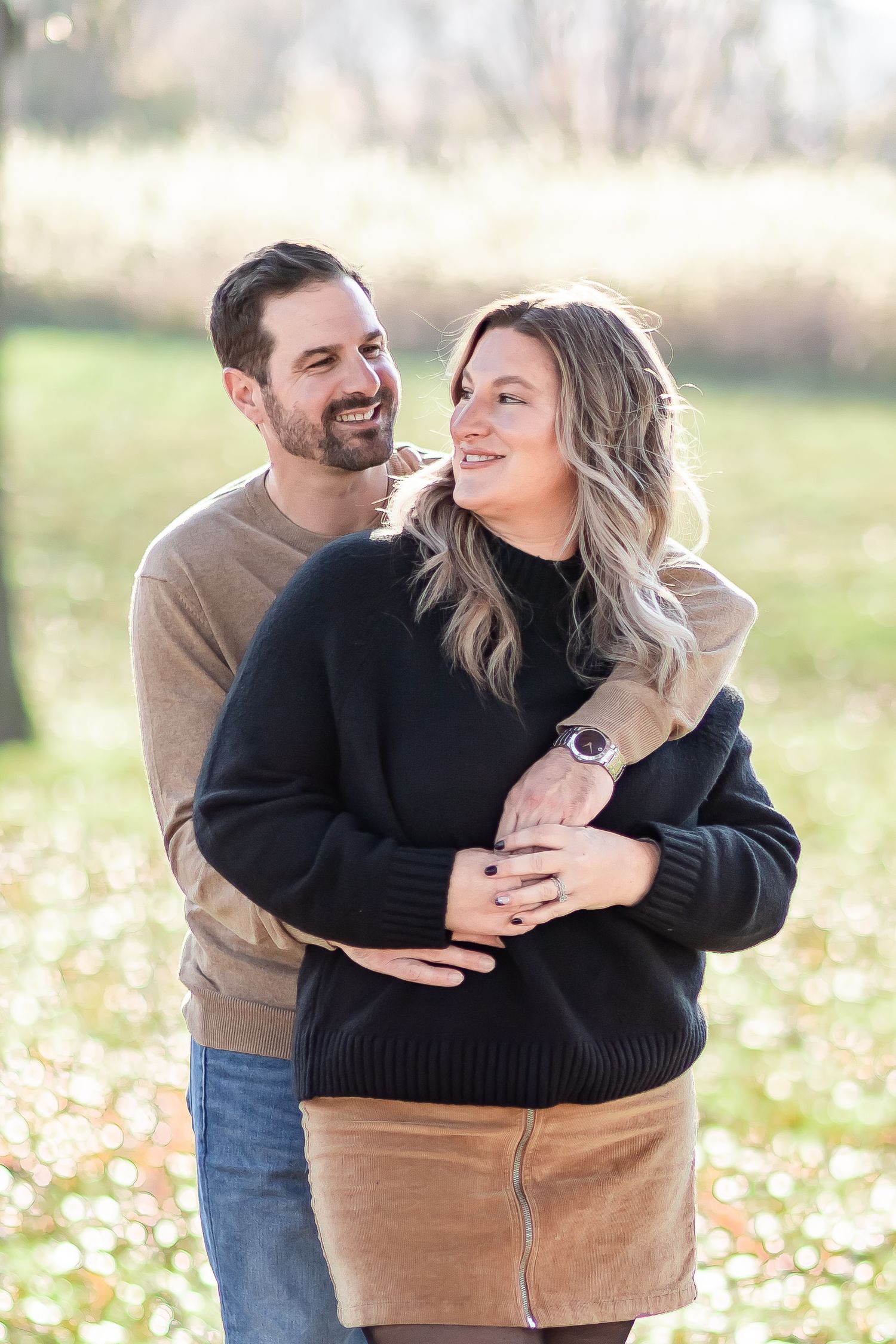 A couple shares joyful moments together in an autumn field with fallen leaves during a photo session.