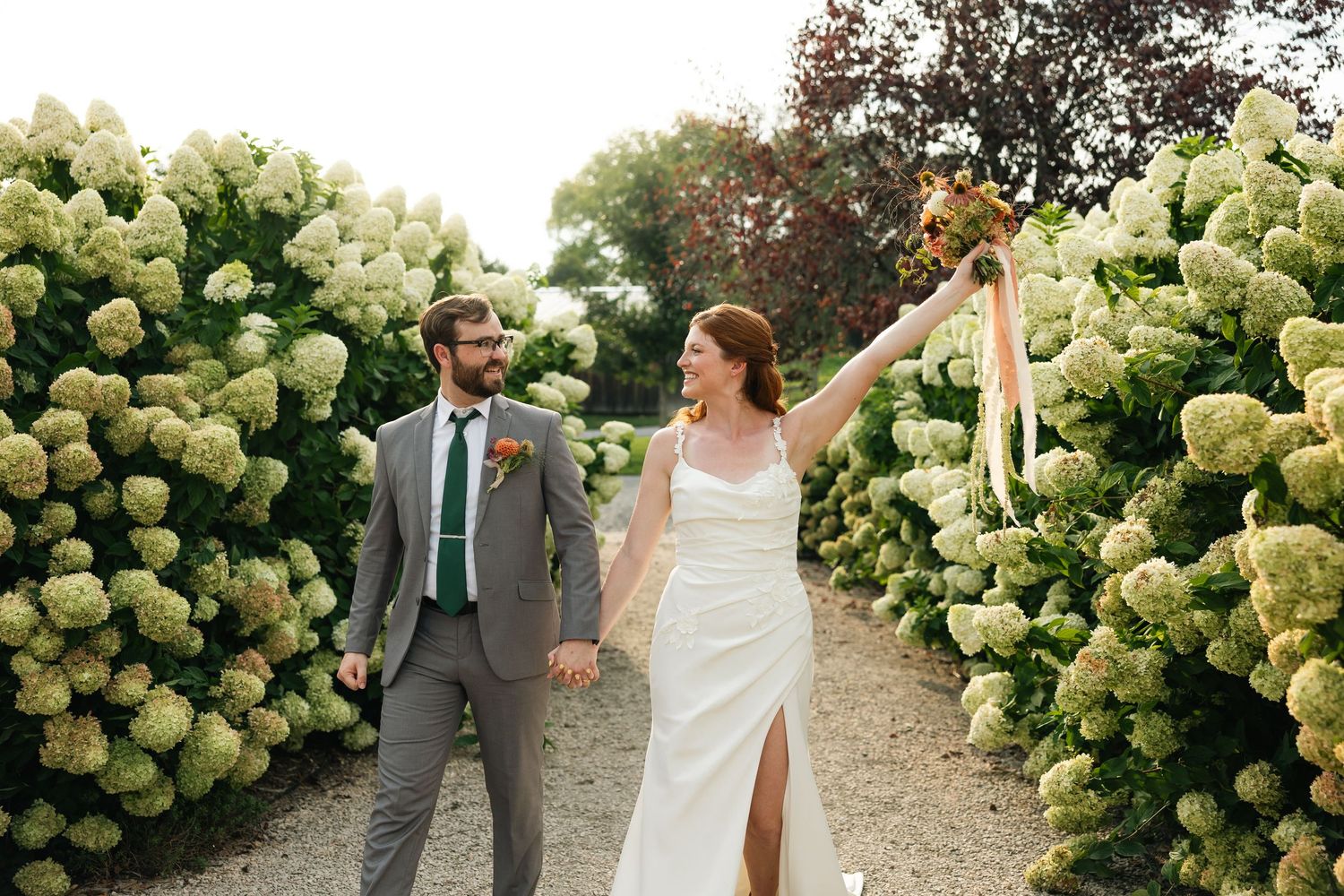 Wedding party poses in front of lush white hydrangea bushes in garden setting.