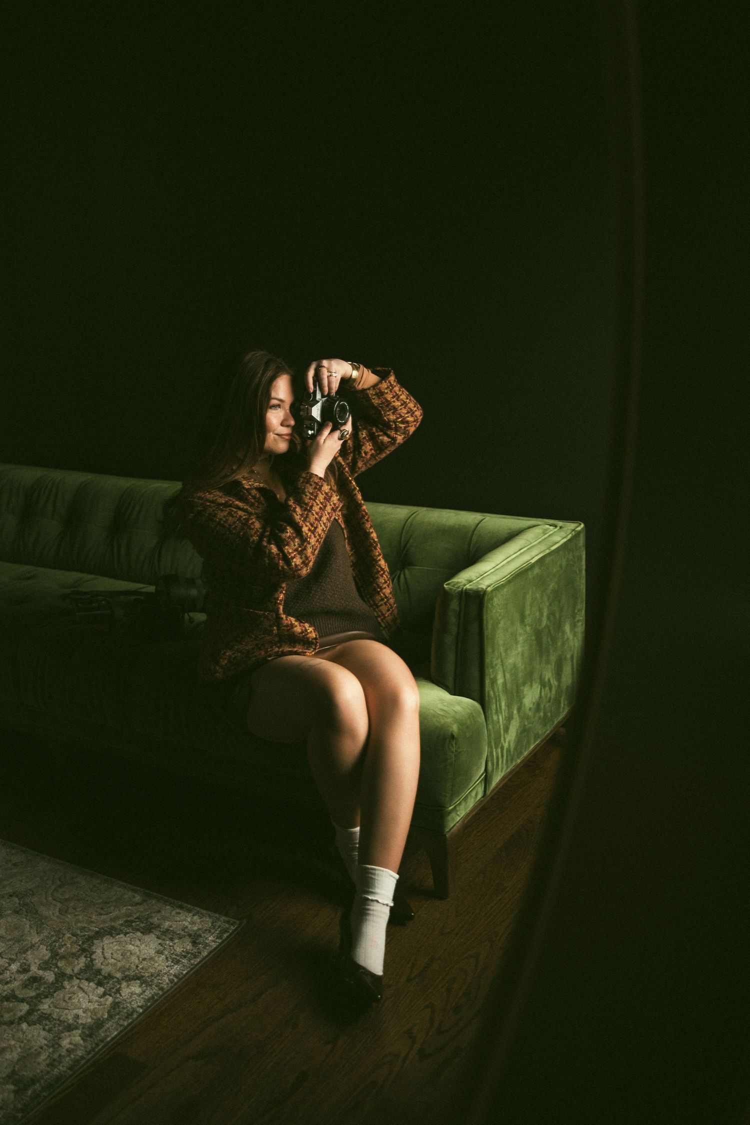 Artistic boudoir photography session on a green velvet couch in moody lighting.