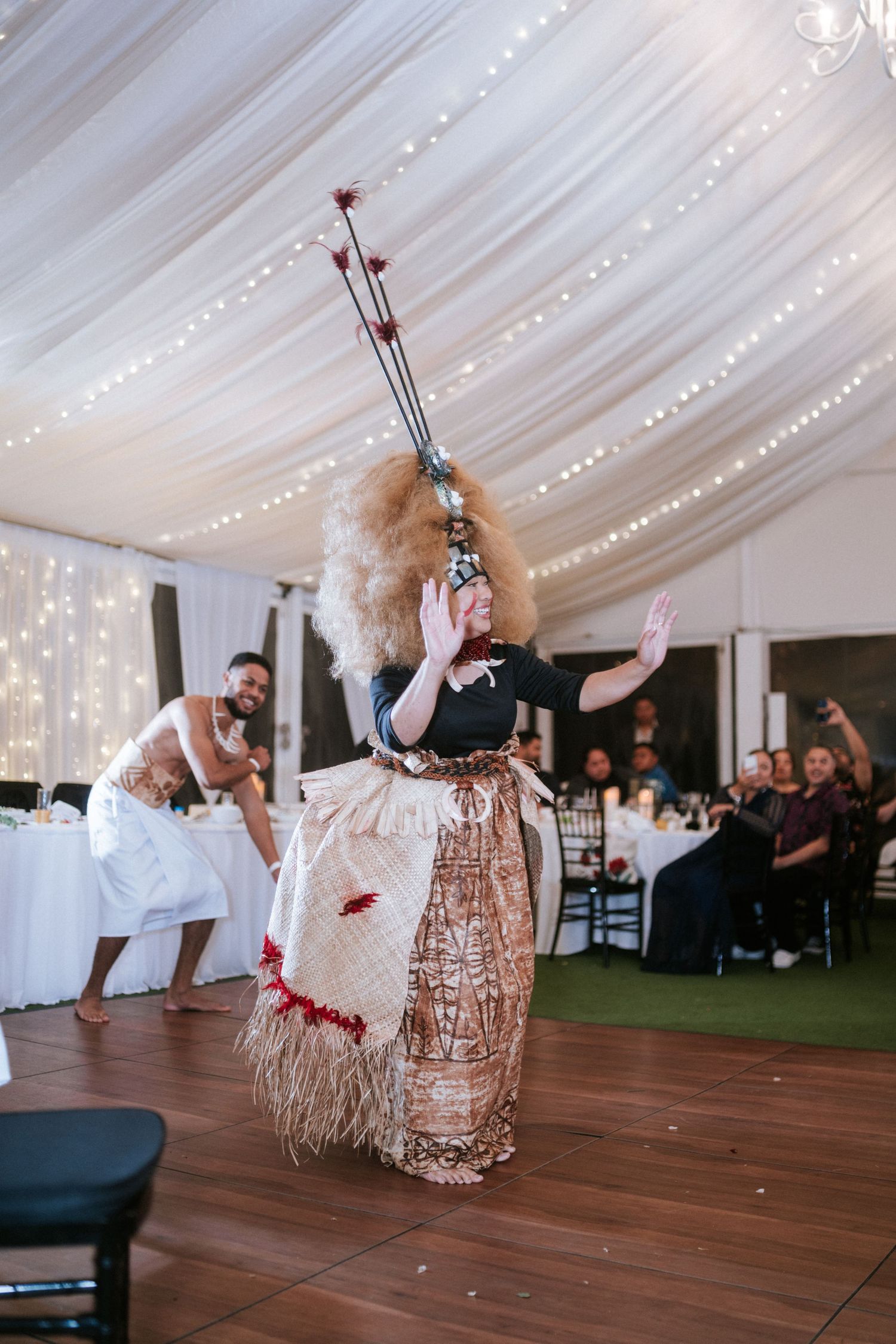 Traditional Polynesian dancer performs in ornate costume at elegant indoor reception with fairy lights.