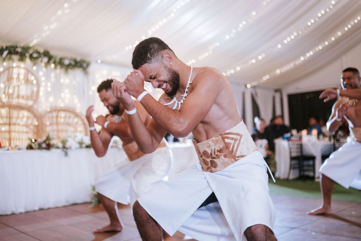 Men in traditional white attire perform a cultural dance at an elegant wedding reception with fairy lights.