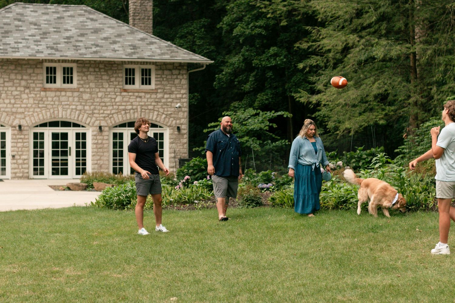 Family playing football with a golden dog in a lush backyard beside a stone house Youngstown Ohio