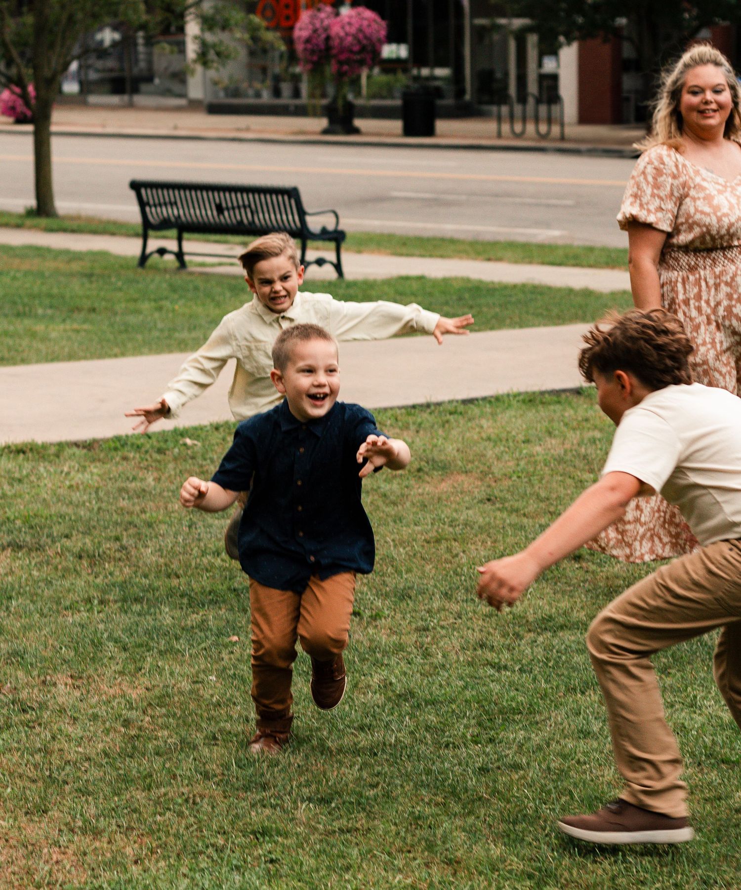 Children play a lively game of tag on a grassy lawn while adults watch in the background.