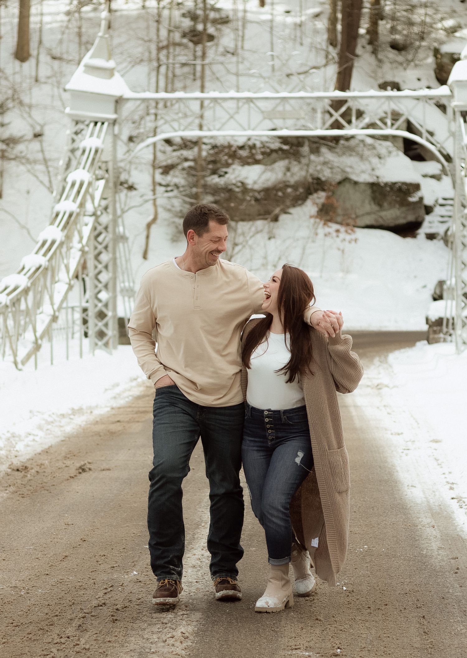 A couple shares a romantic moment walking together on a snowy winter path in matching beige sweaters.