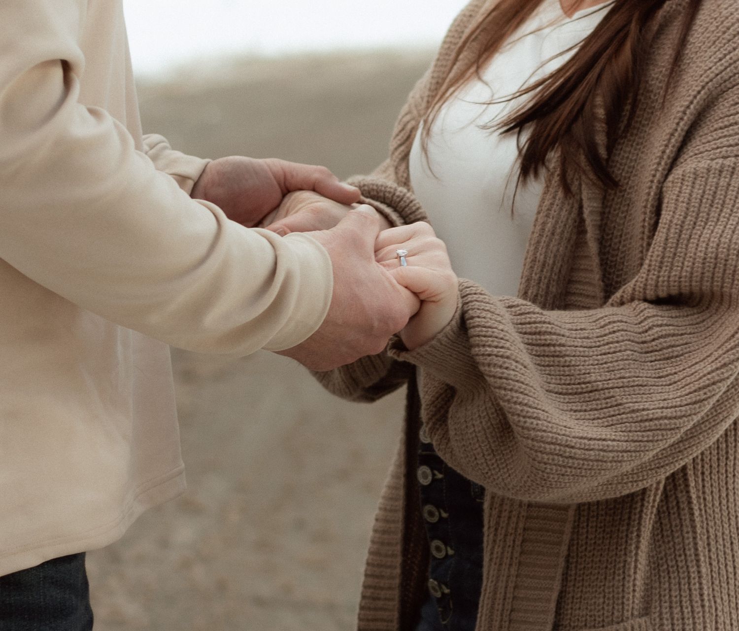 Close-up of hands holding each other in comfort against neutral beige sweater background.