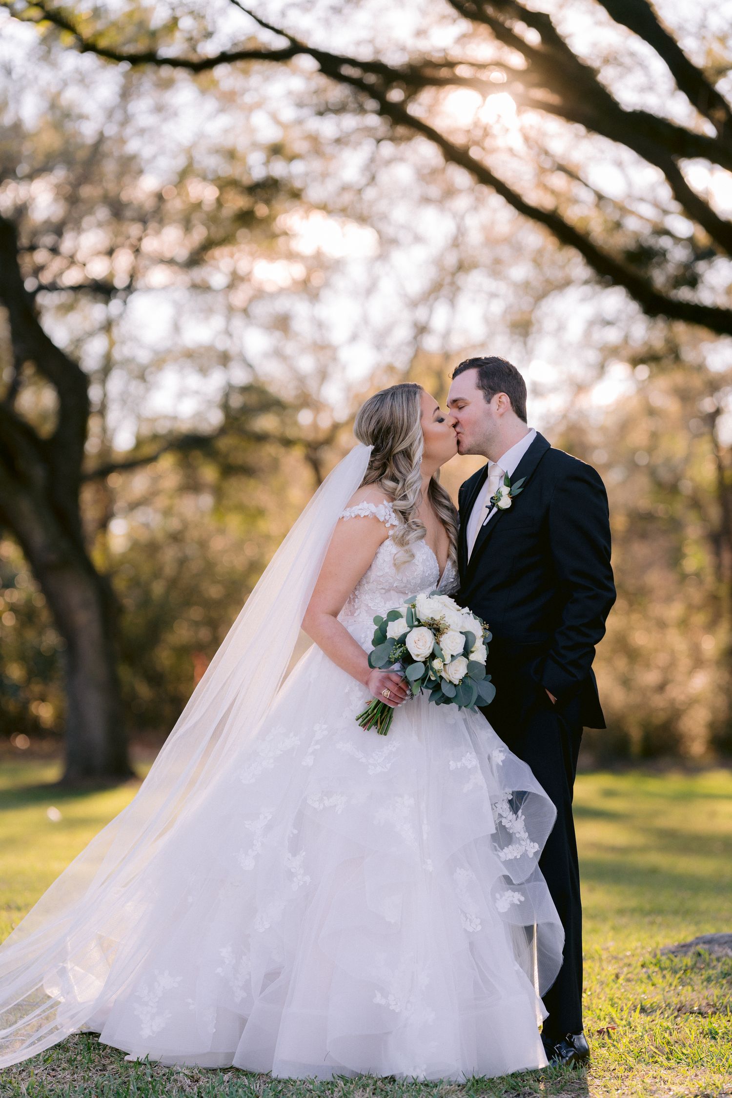 Romantic wedding portrait under blooming trees in golden sunlight.