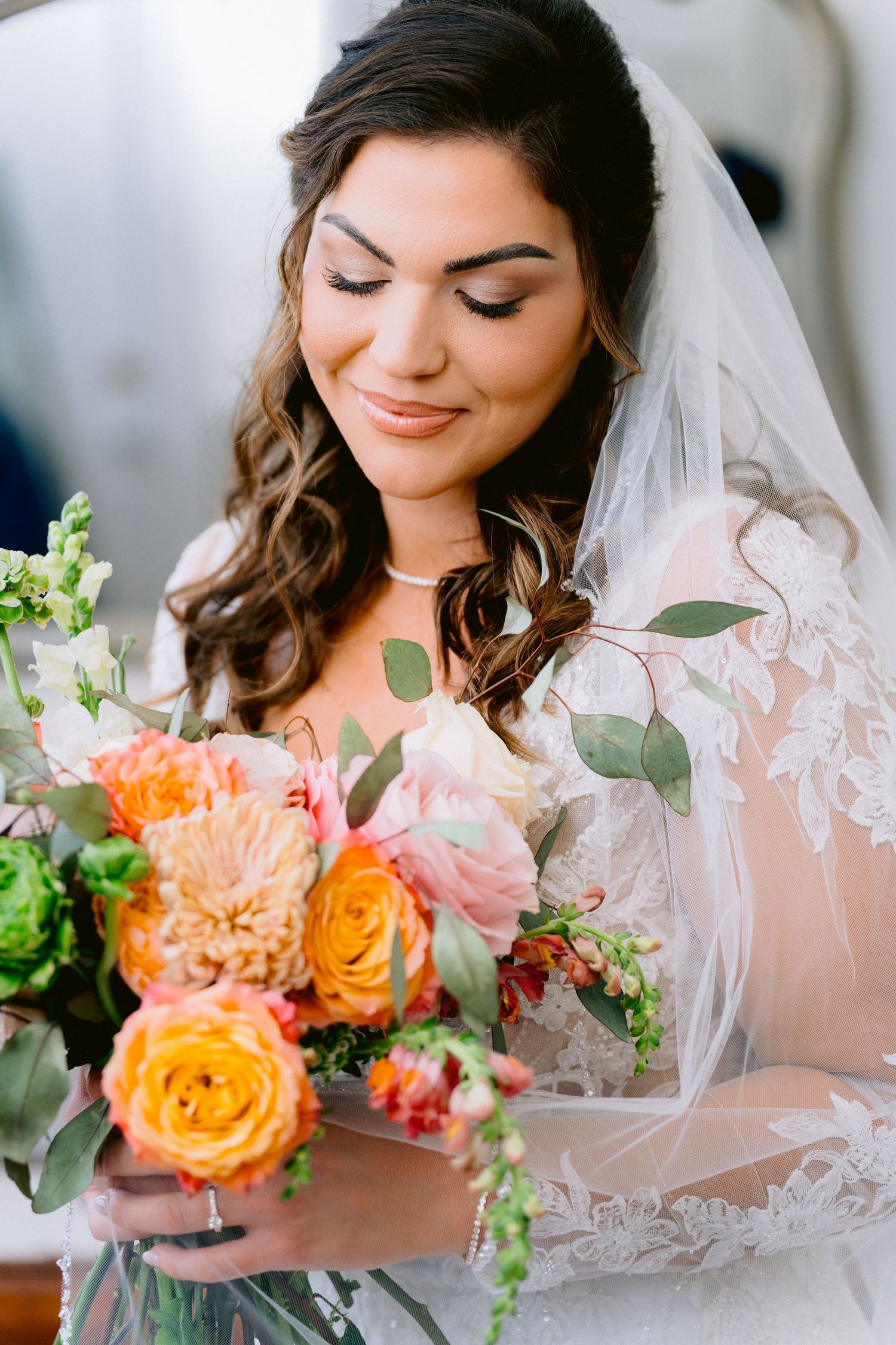 A bride in white veil holds a stunning bouquet with peach roses, dahlias and eucalyptus greenery. Tampa Wedding Photographer