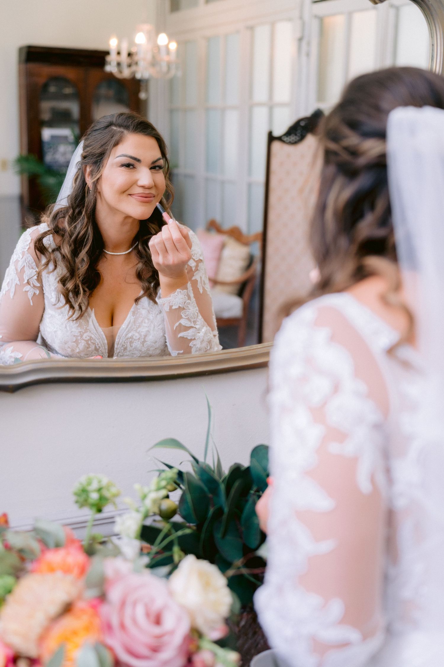 Bride looks in the mirror while getting ready on her wedding day, surrounded by soft lighting and romantic decor. Tampa Wedding Photographer