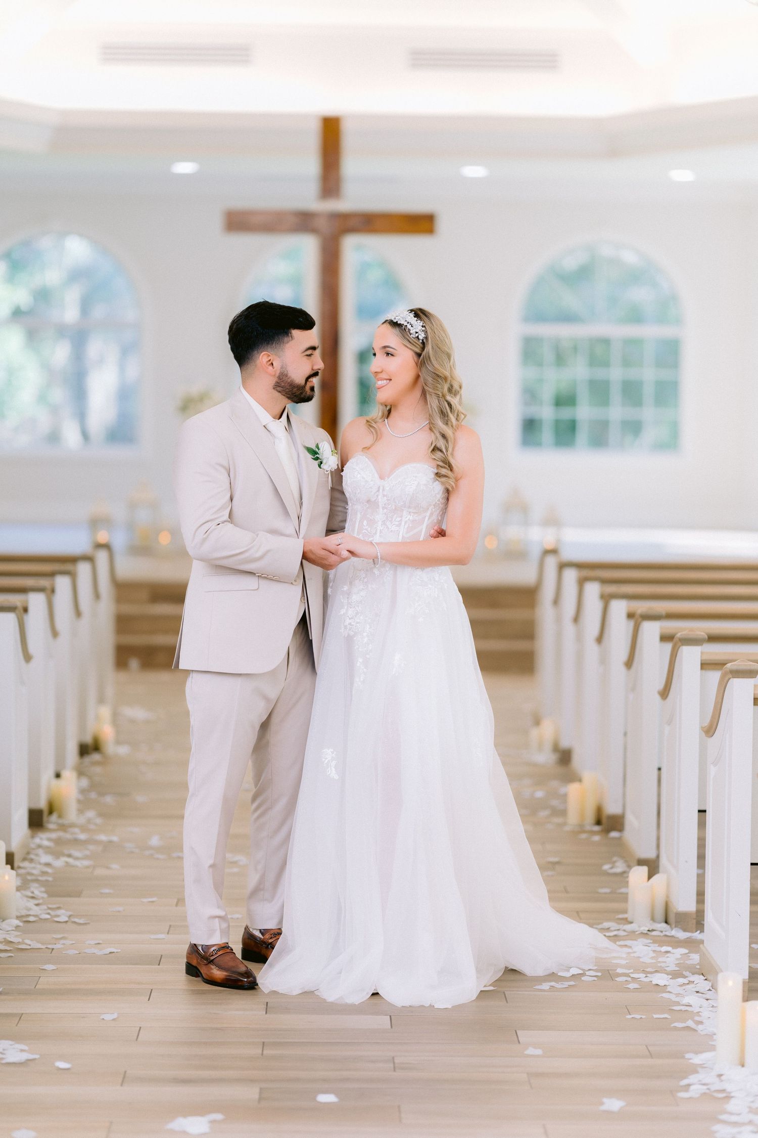 A bride and groom share a romantic moment in a bright white chapel with wooden pews and a cross in the background. Tampa Wedding Photographe