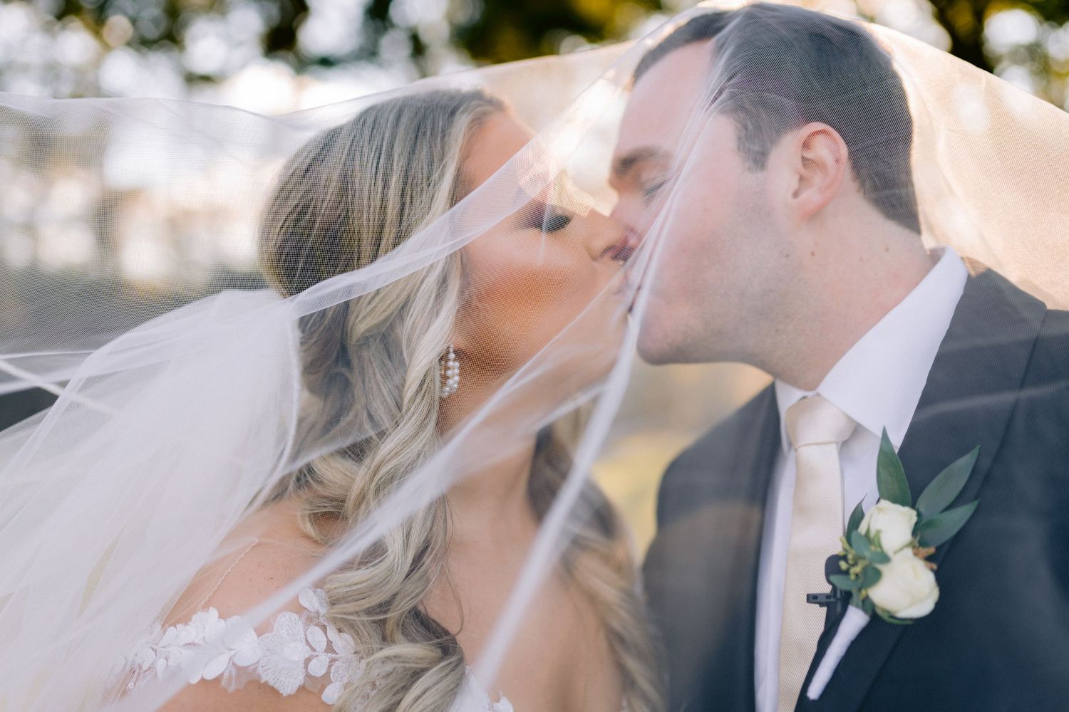 Wedding portrait shows a tender kiss between newlyweds with a flowing white veil in soft natural light. Tampa Wedding Photographer