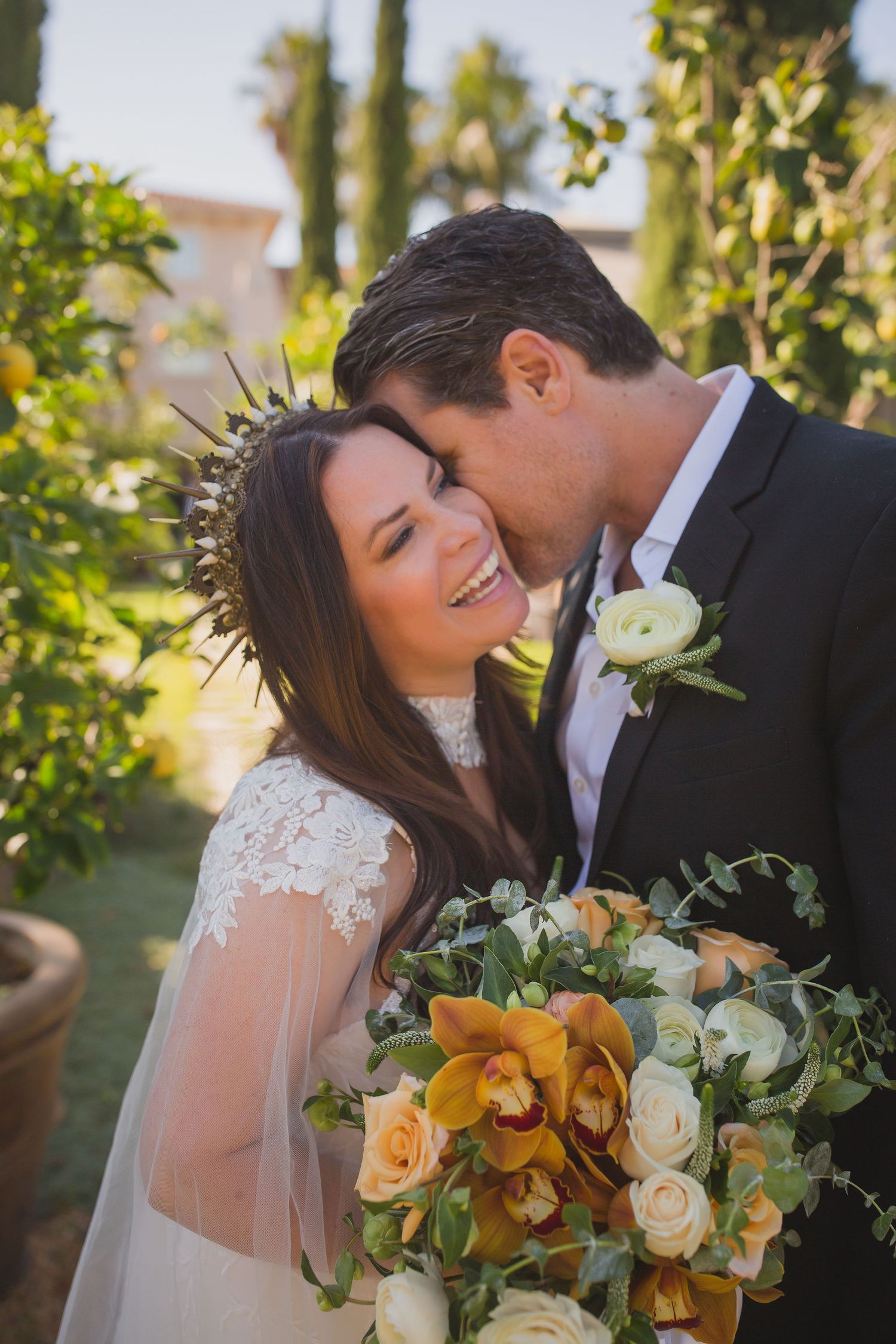 A romantic wedding couple shares intimate moments in a garden setting with white and orange floral bouquets.