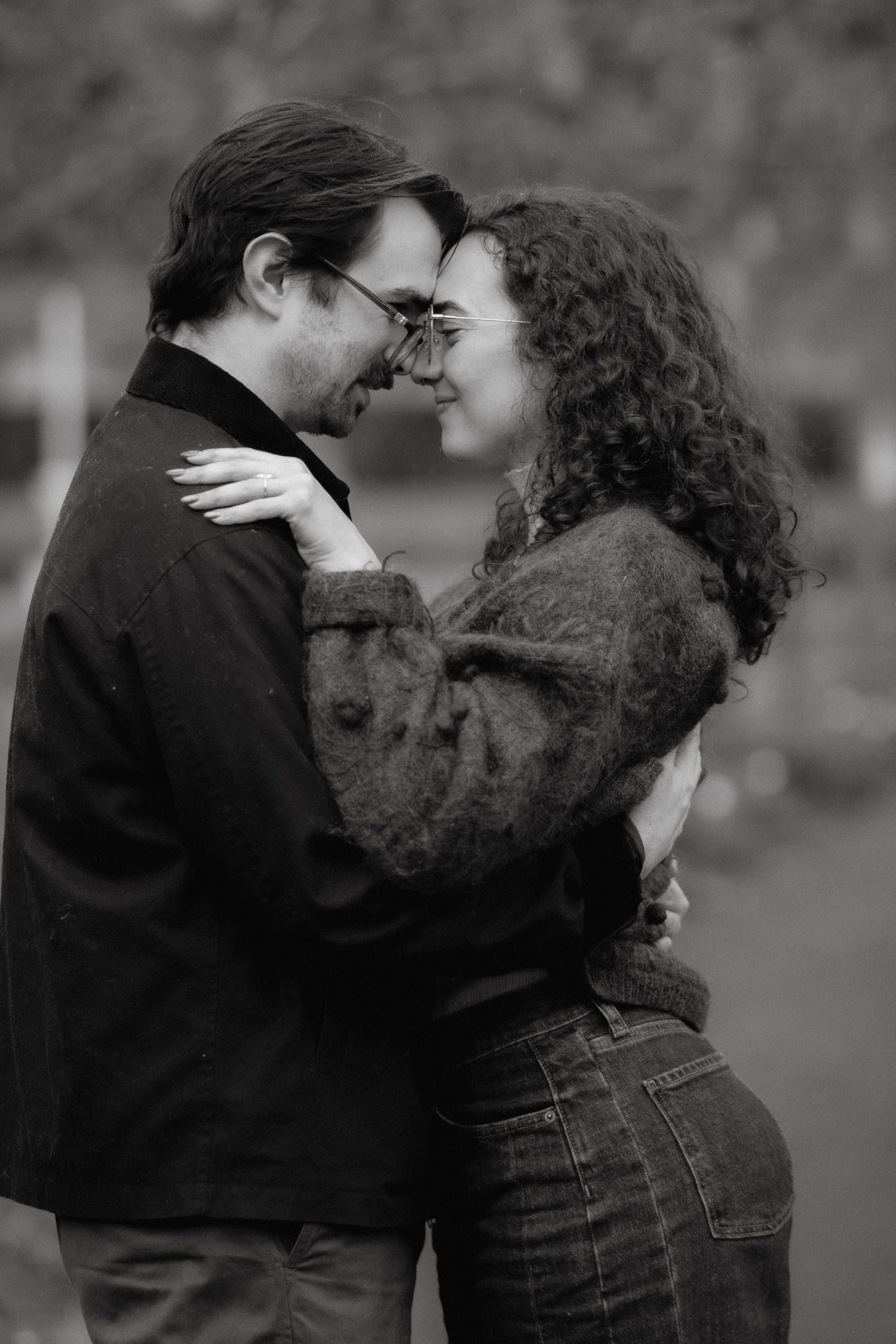 Black and white photo of a romantic couple embracing outdoors, touching foreheads and smiling at each other.