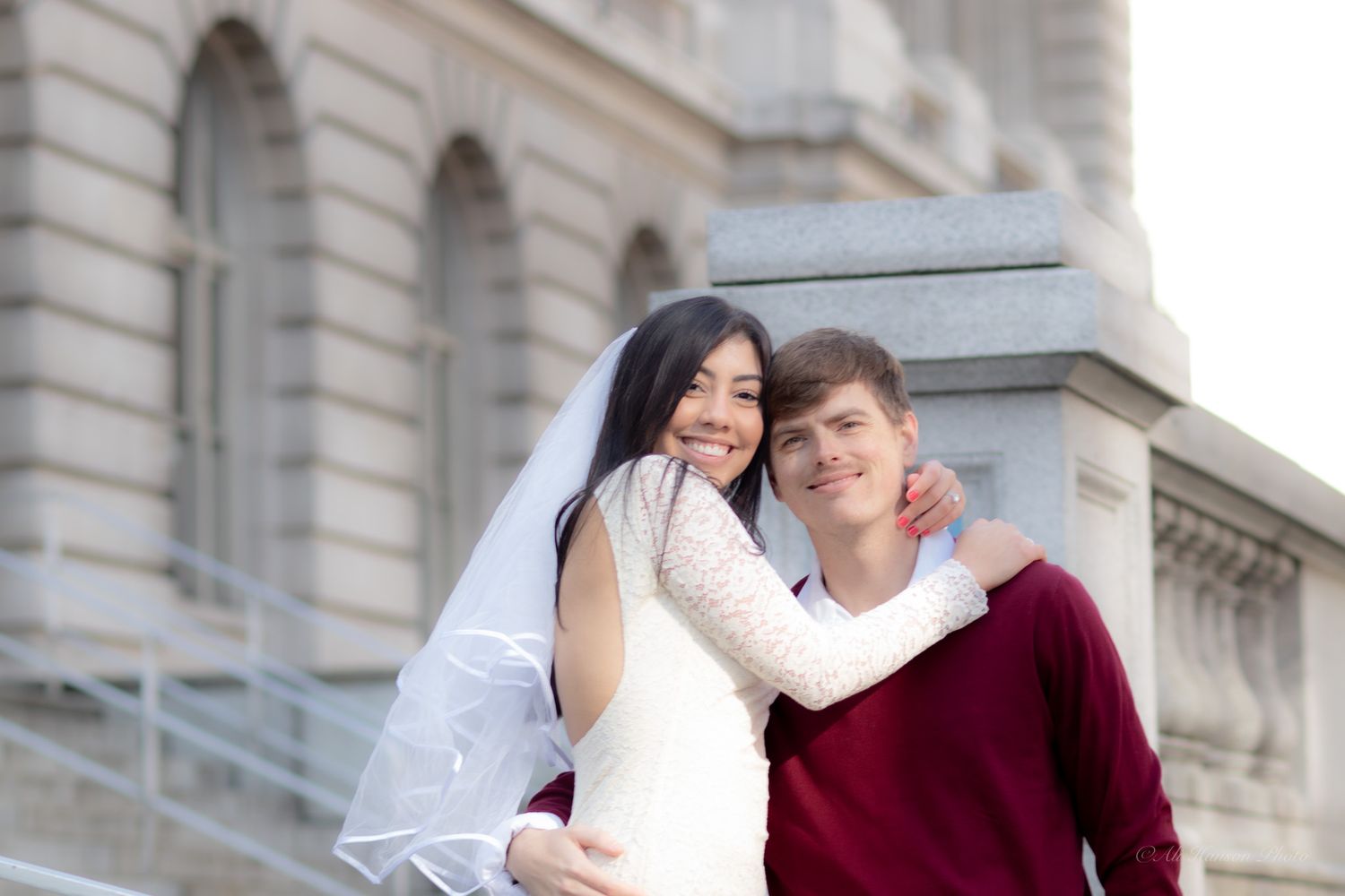 A young couple in wedding attire poses in Tacoma WA courthouse, bride in white dress and veil, groom in red sweater.