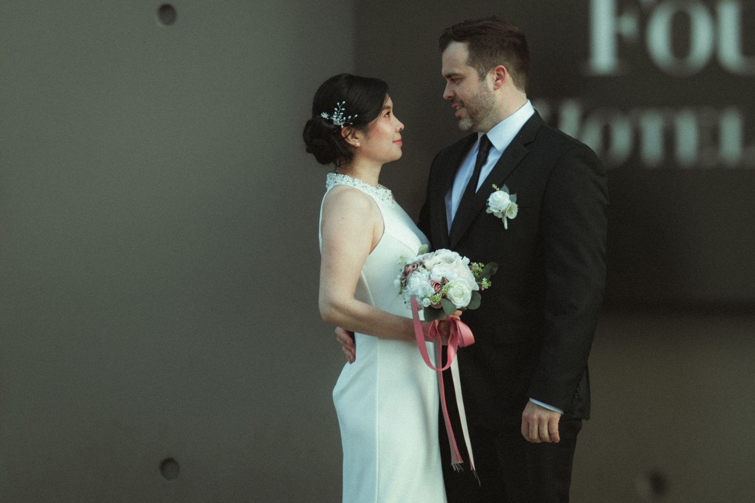 Bride and groom share a romantic moment holding a bouquet at a wedding venue.