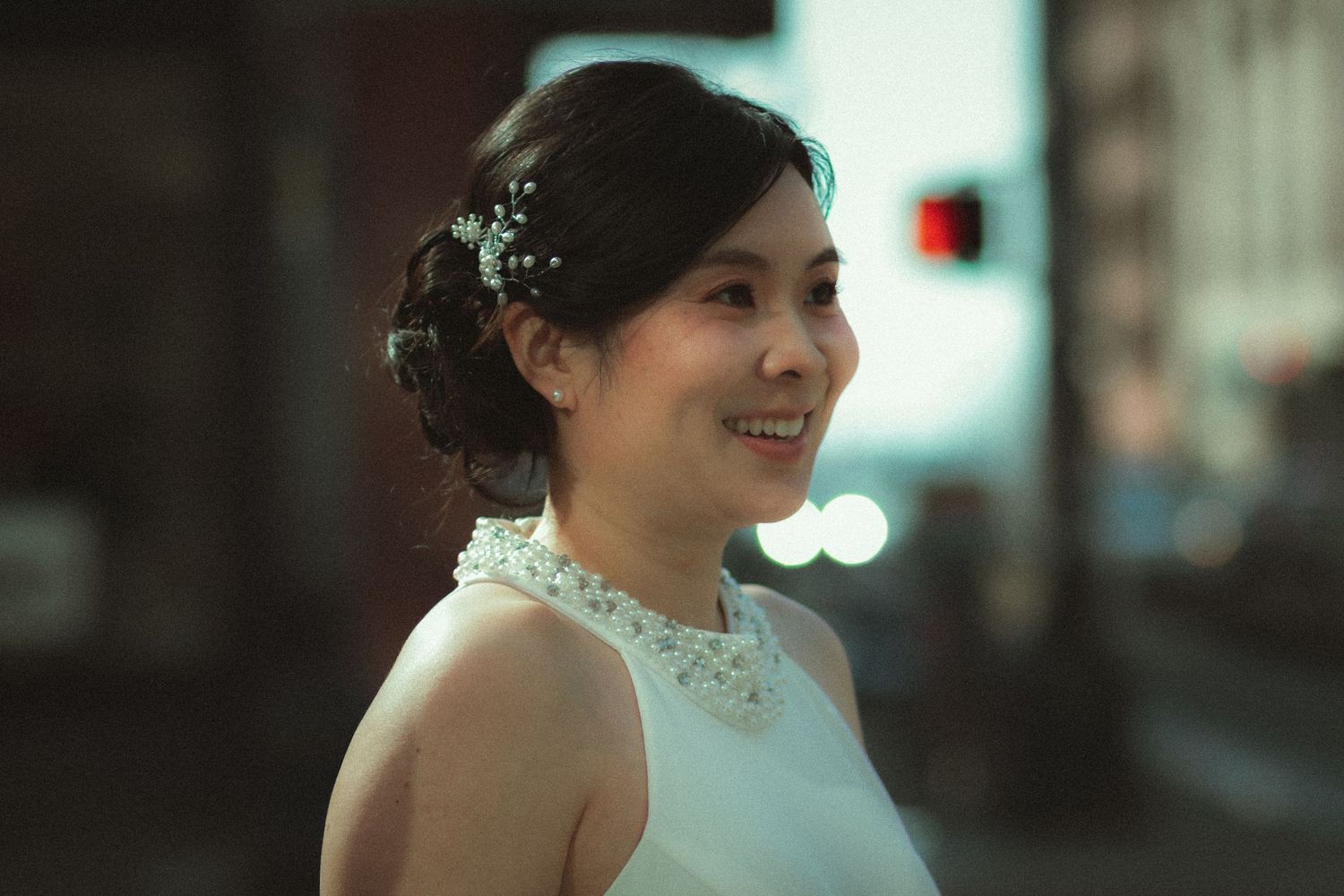 A smiling woman in a white halter wedding dress with pearl neckline and floral hair accessories on a Seattle street.