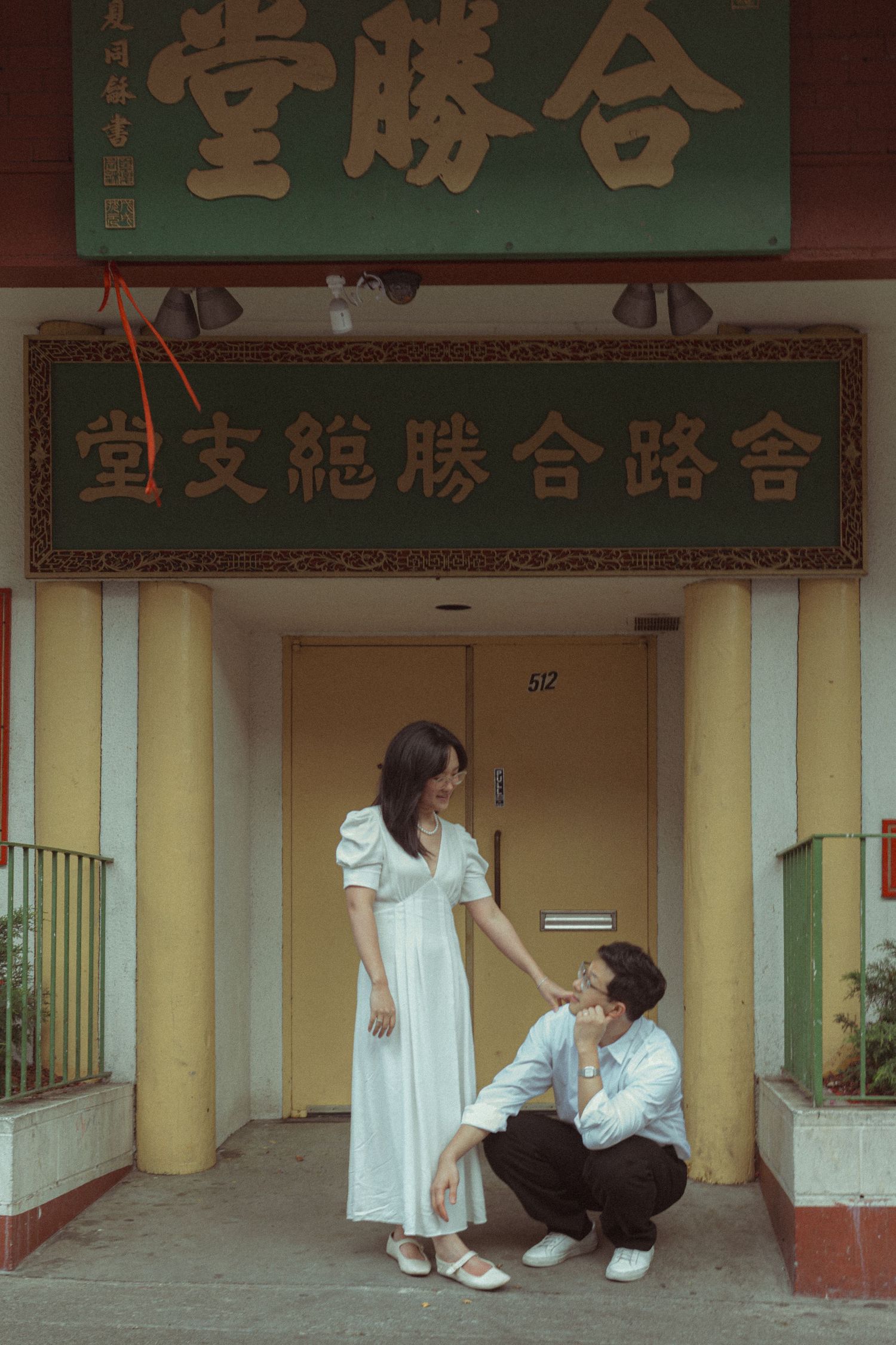 Couple in white outfits pose romantically at a traditional Chinese building entrance with green signage.