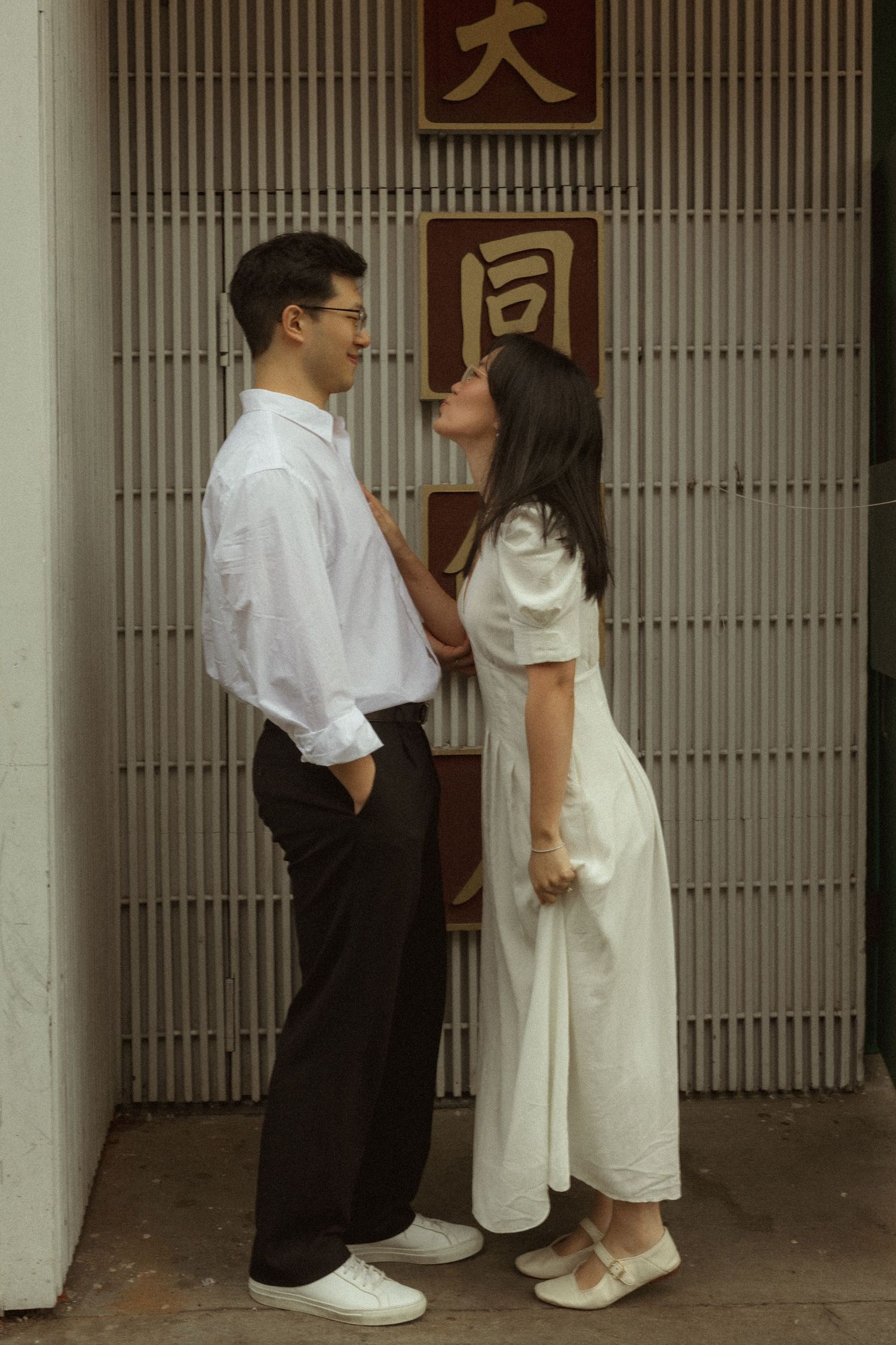 Couple in white outfits sharing a romantic moment outside a building with Chinese characters.