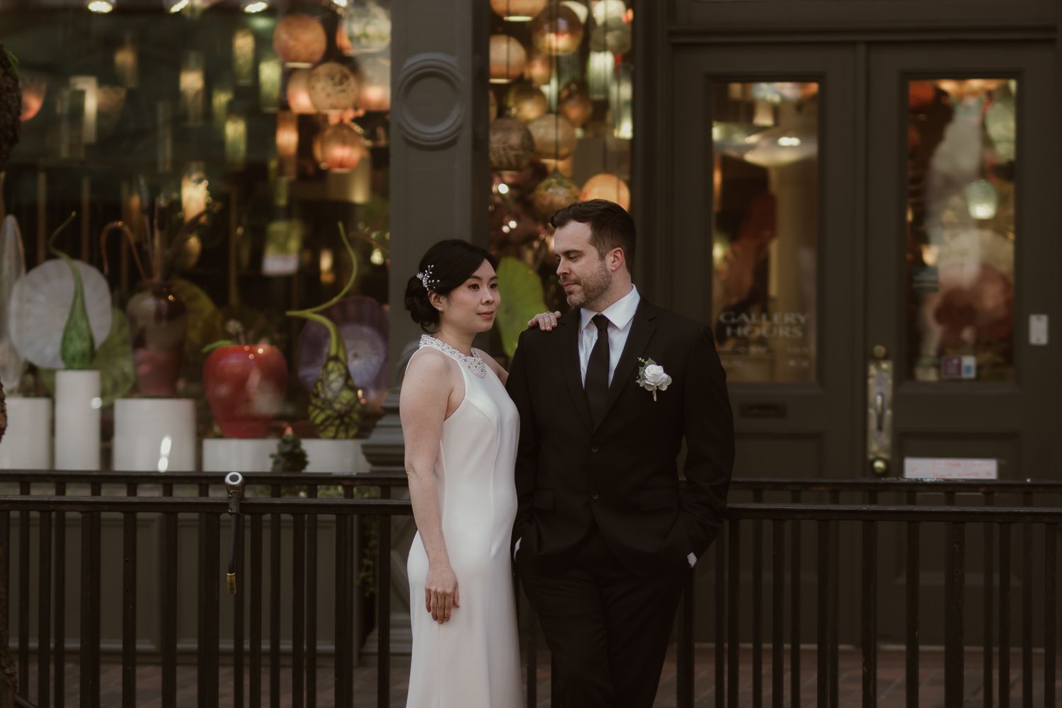 Bride and groom stand together outside Downtown Seattle in a warmly lit venue with colorful lanterns and decor in the background.