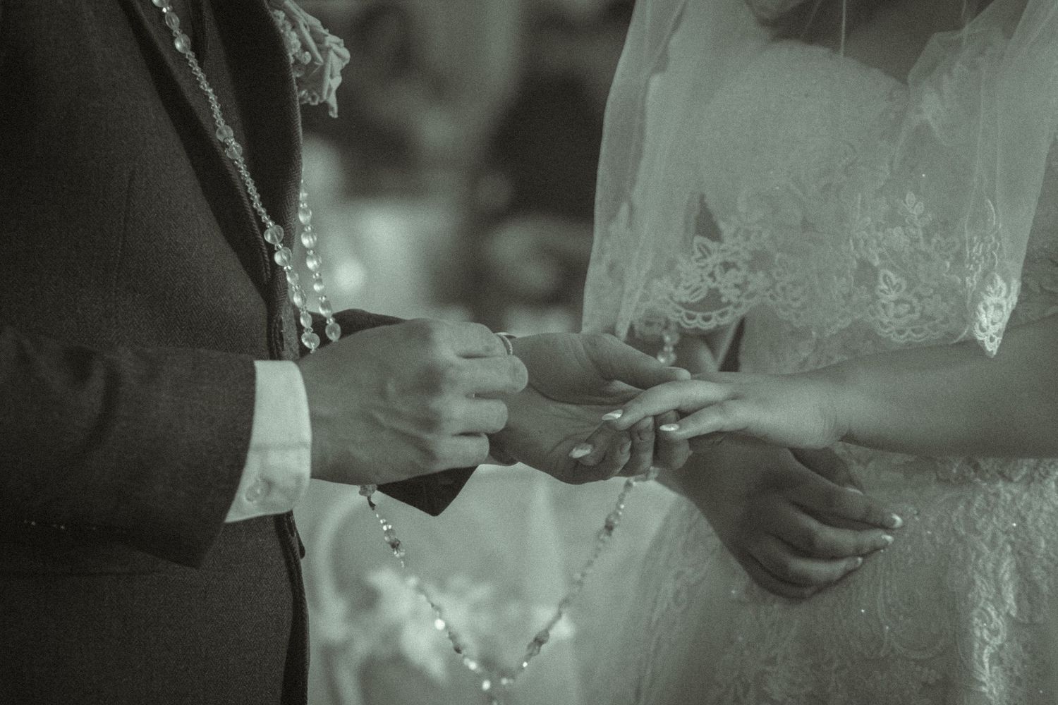 Black and white photo of a couple exchanging wedding rings during a marriage ceremony.