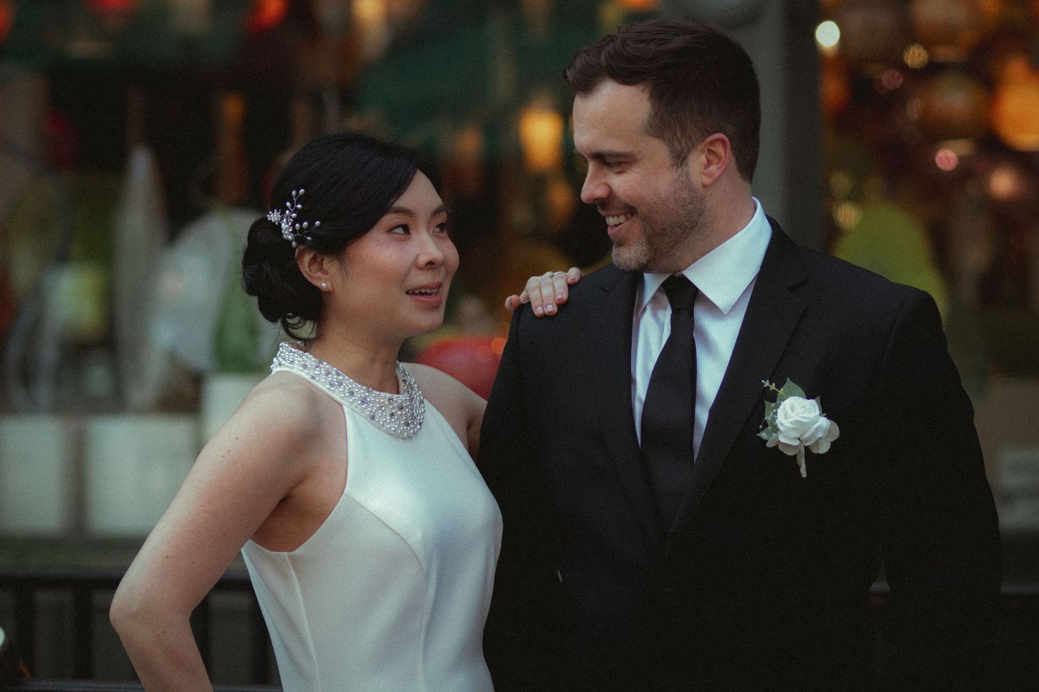 Bride and groom in elegant wedding attire smiling at each other outdoors at a romantic evening venue Seattle.
