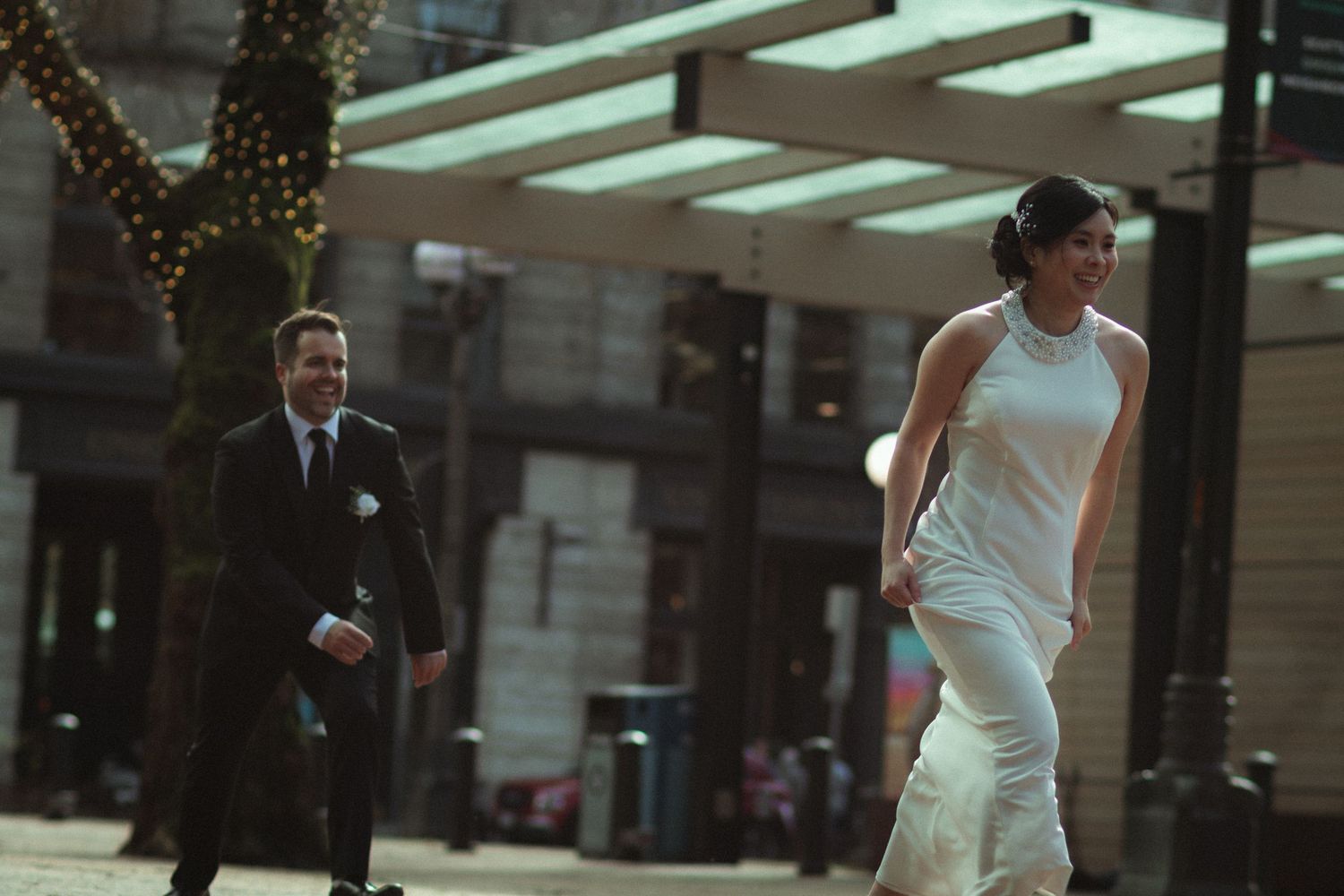 A bride in a white gown and groom in a suit walk through an urban plaza during a wedding photo session.