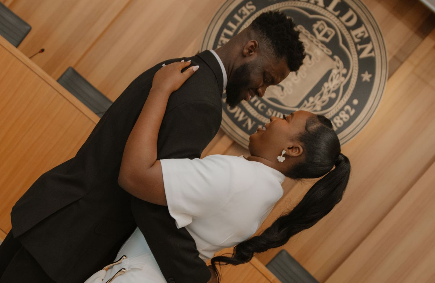 Couple dancing together on a wooden floor with a circular logo.