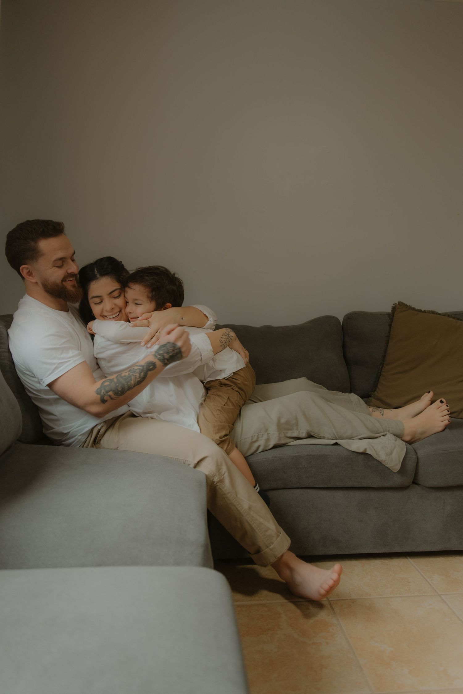 A happy family of three cuddling together on a gray couch in a cozy living room.