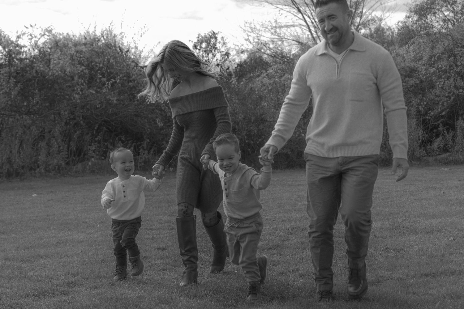 Black and white photo of a happy family with two young children holding hands and walking together on a grassy field.