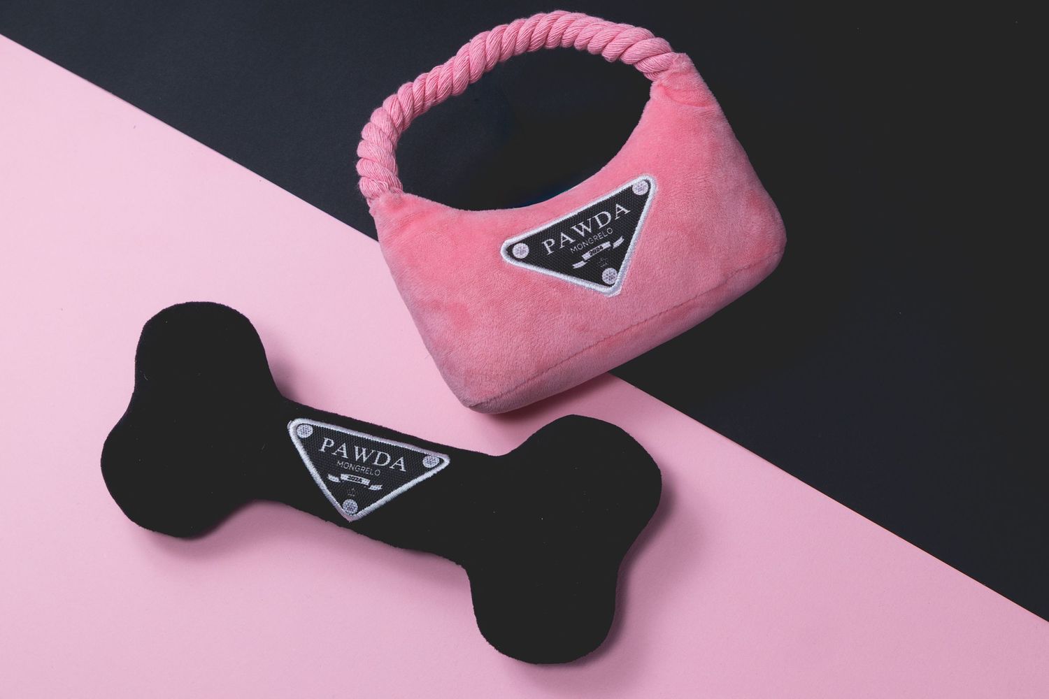 “Flat-lay of pink handbag-shaped dog toy and black bone toy on a split pink and black background.