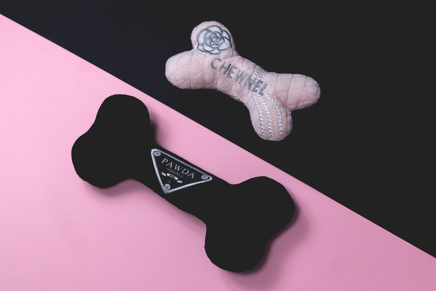Flat-lay of two bone-shaped dog toys on a split pink and black background, one light and one dark.
