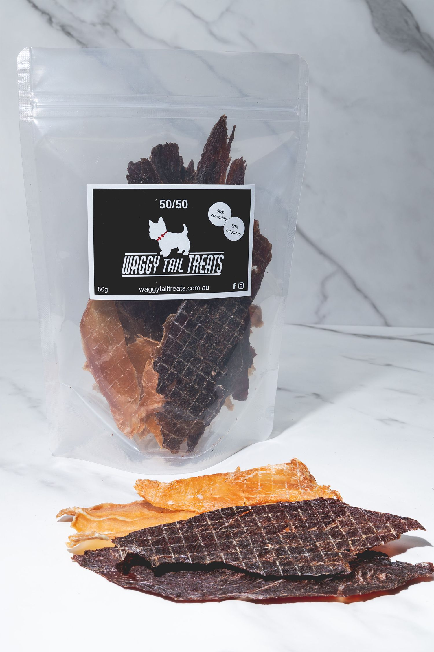 Studio product shot of a clear bag of dog jerky treats, with individual pieces arranged in front on a white marble surface.