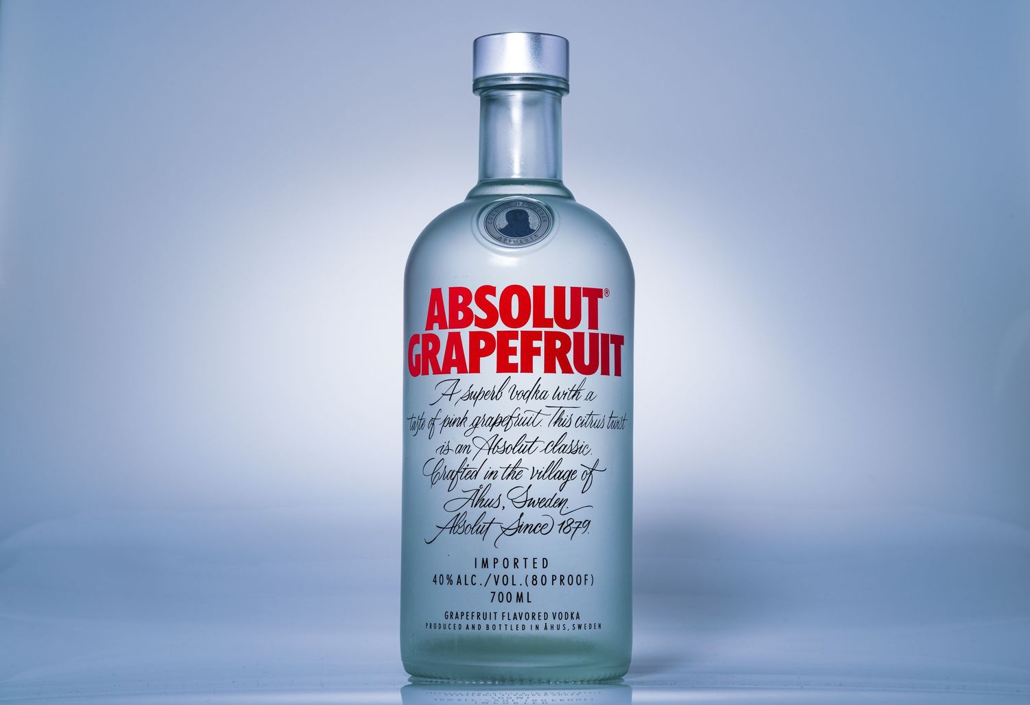 Studio product photograph of an Absolut Grapefruit vodka bottle on a cool blue gradient background.