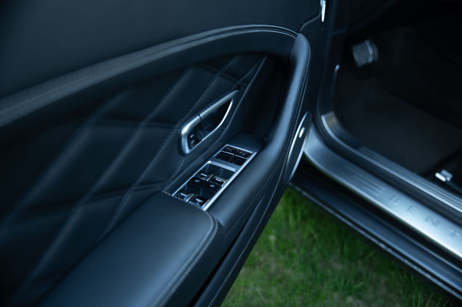 Black quilted leather door panel of a Bentley Continental GT with chrome window controls and trim.
