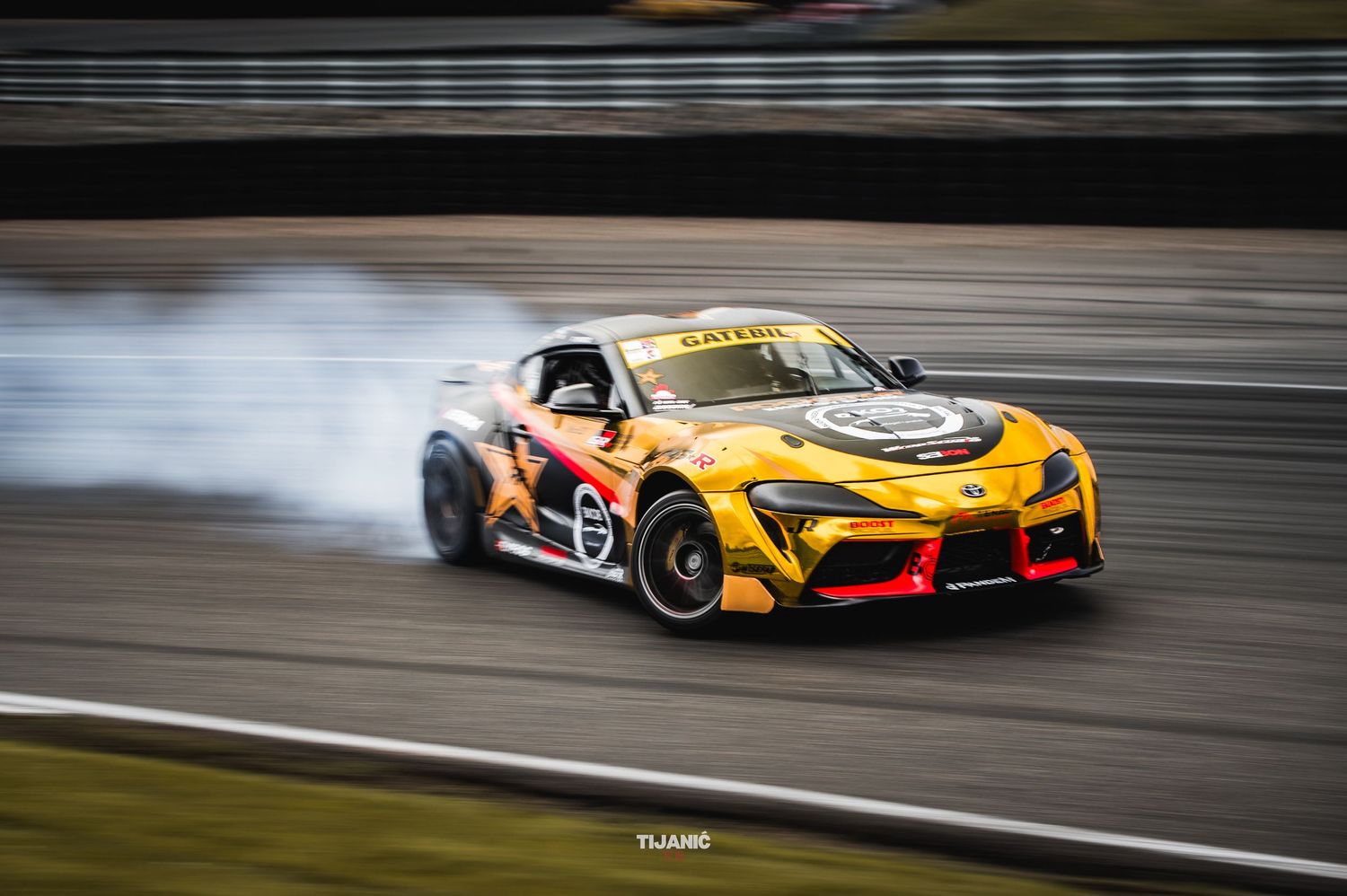 Yellow Red Bull sponsored Toyota GR Supra racing car drifting with heavy tire smoke on track.