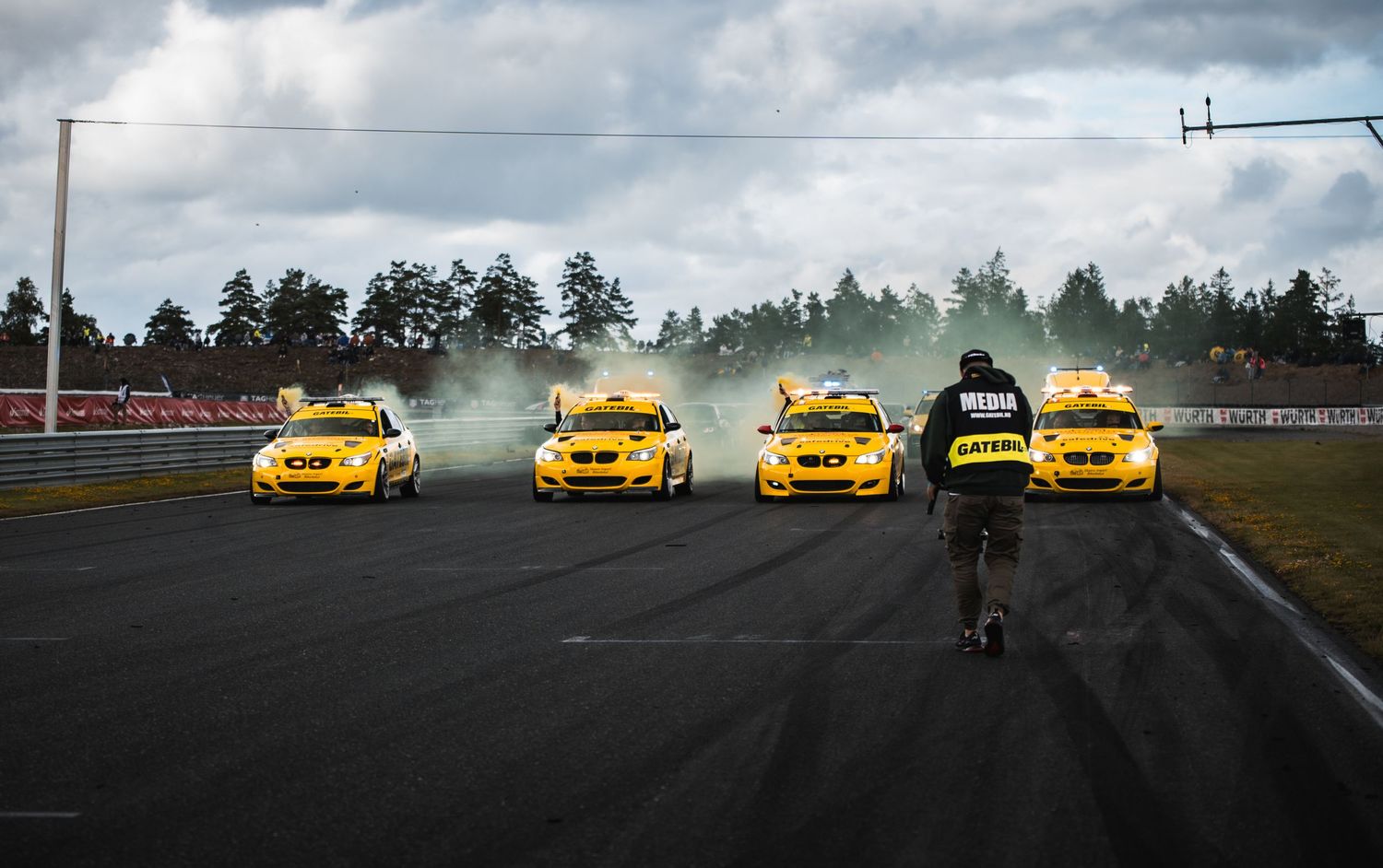 Four yellow BMW drift cars lined up producing smoke on a motorsport circuit.