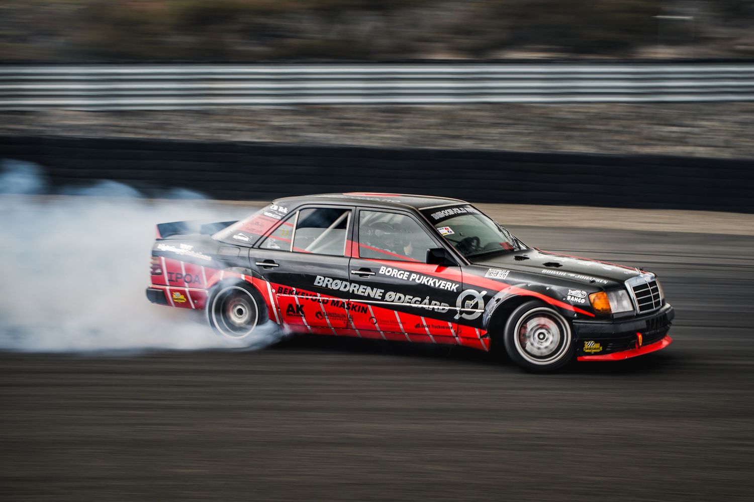 Black and red Mercedes-Benz drift car sliding with smoke on a motorsport circuit.