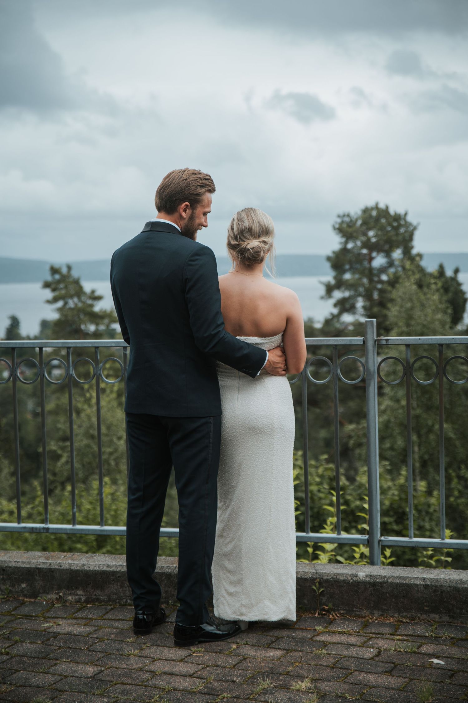 Bride and groom standing together at a railing overlooking a scenic lake on their wedding day.