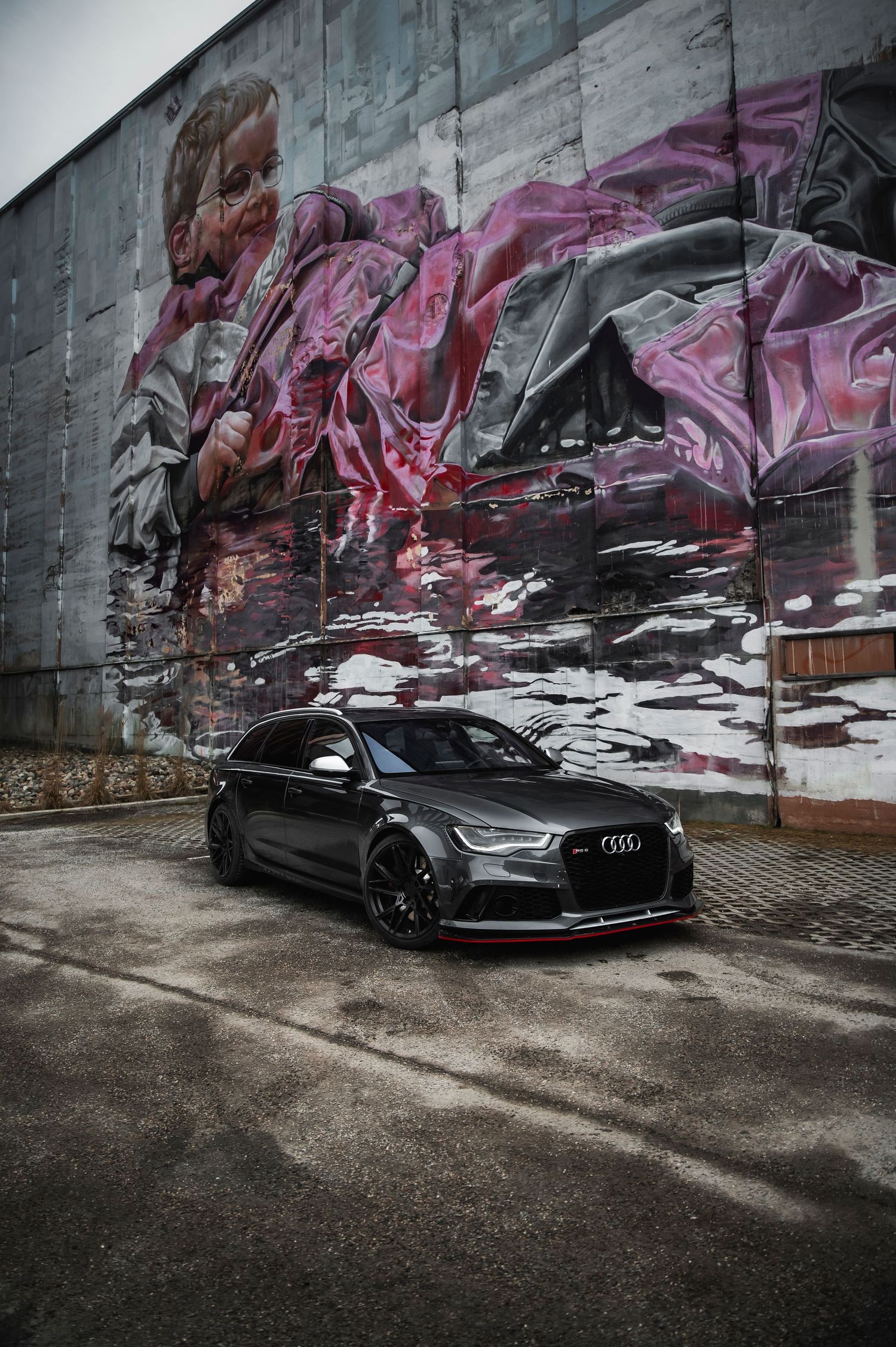 Matte black Audi RS6 Avant parked in front of a large colorful graffiti mural.