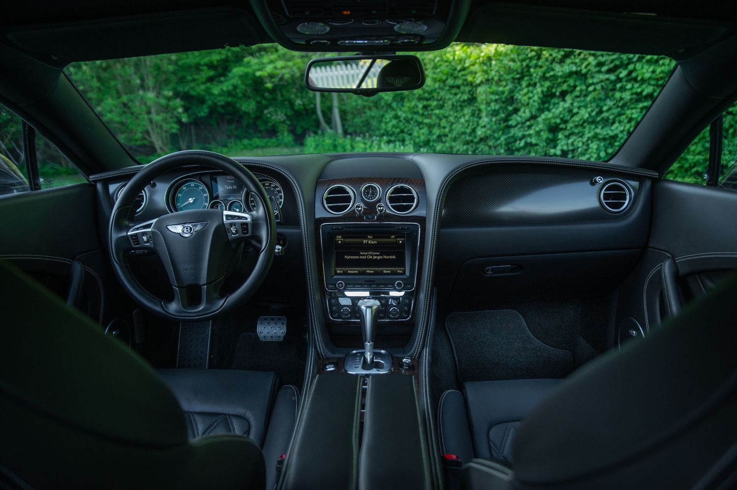 Luxurious Bentley Continental GT interior featuring black leather dashboard, analog gauges and center console.