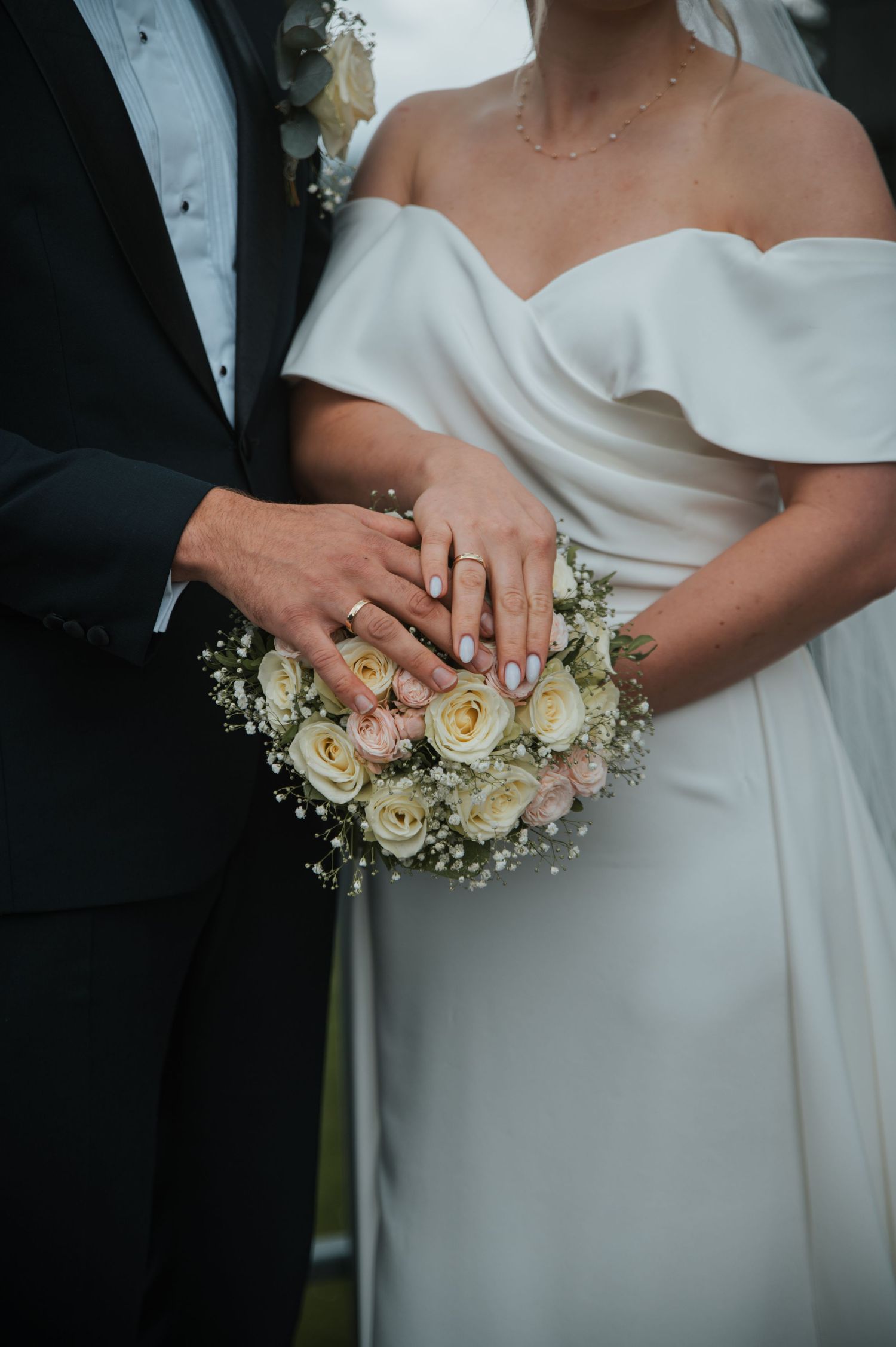 Close-up of bride and groom displaying wedding rings resting on a white rose and baby's breath bouquet.