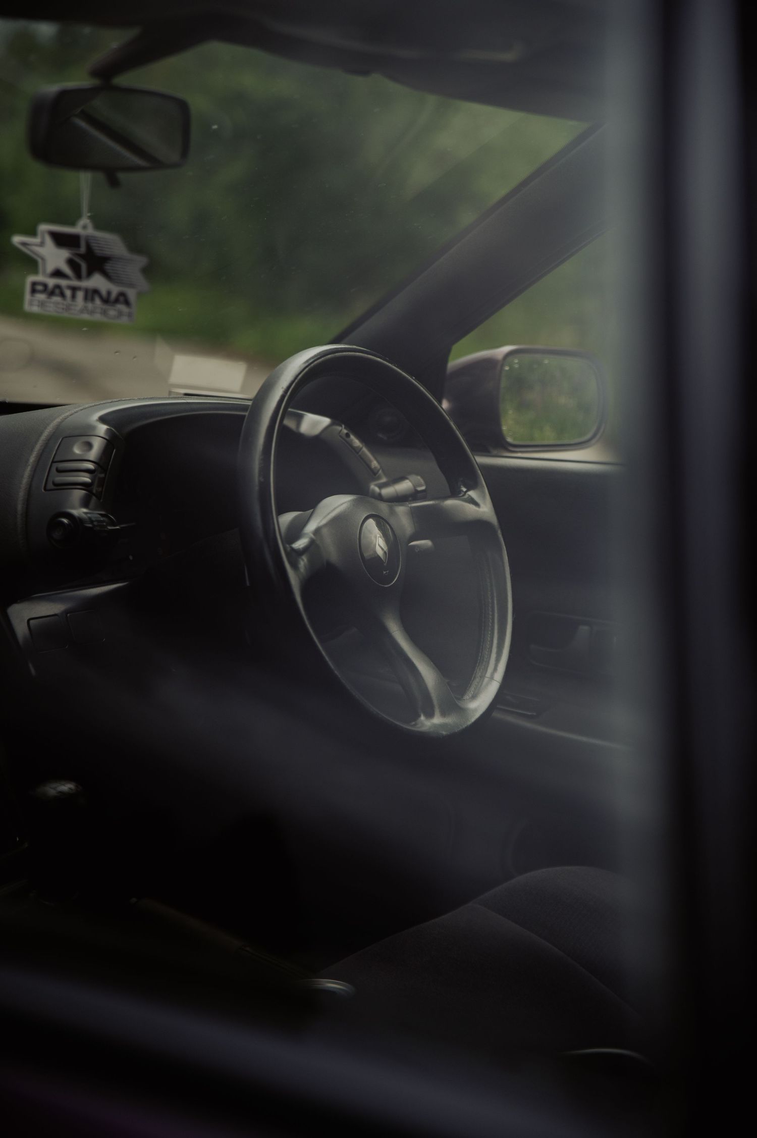 Interior view of a modified Japanese sports car featuring a aftermarket steering wheel and Patina air freshener.