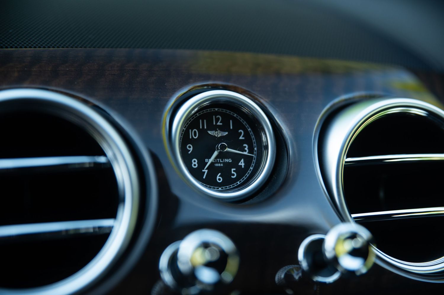 Close-up of a Breitling analog clock on a Bentley Continental GT dashboard between chrome air vents.