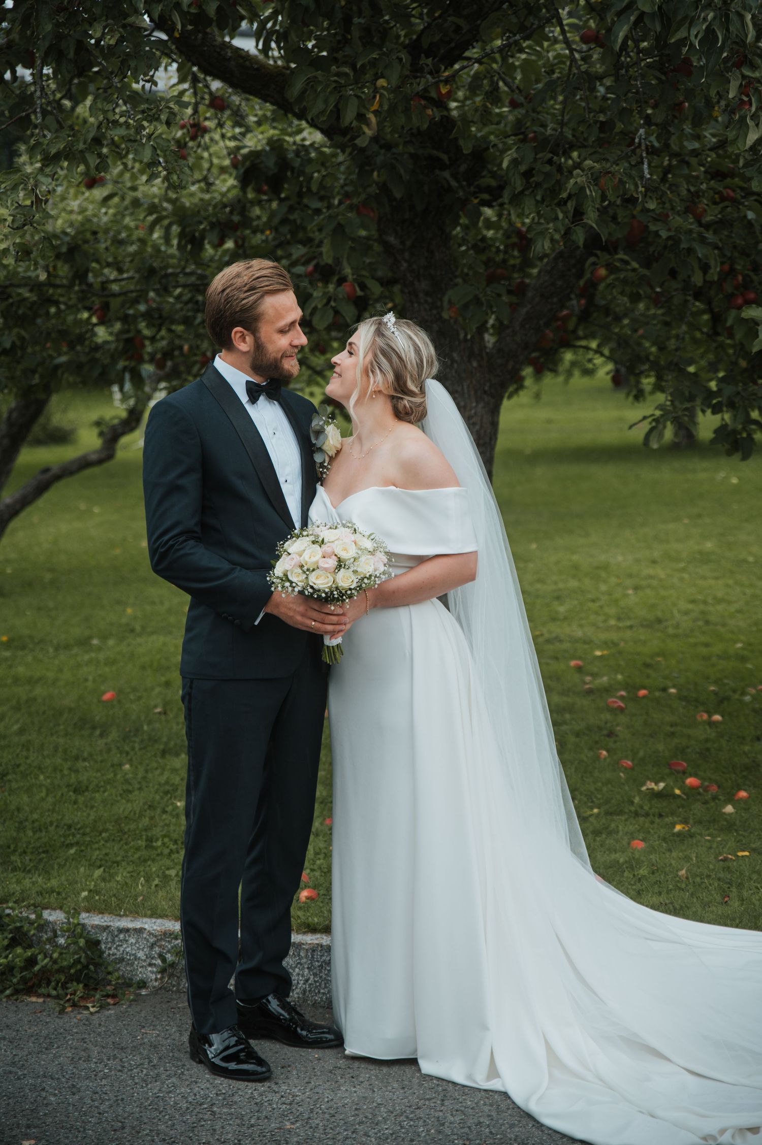 Bride and groom sharing a romantic moment under an apple tree in a lush garden.