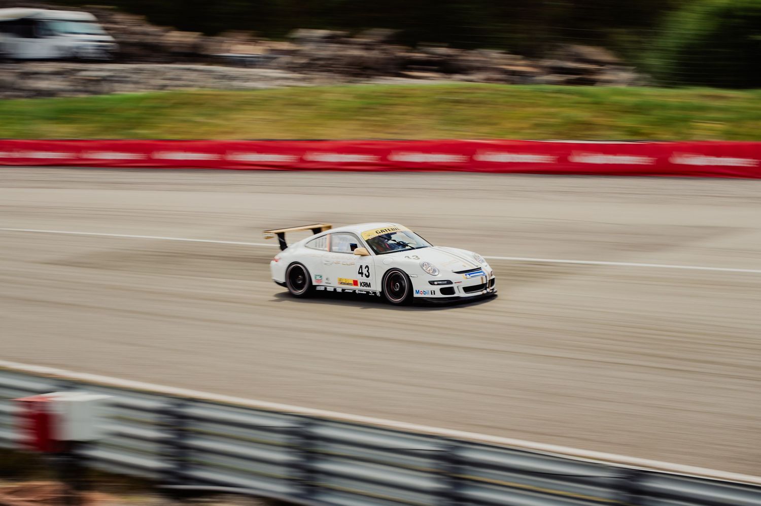 White Porsche 911 GT3 race car number 43 speeding on track with motion blur.