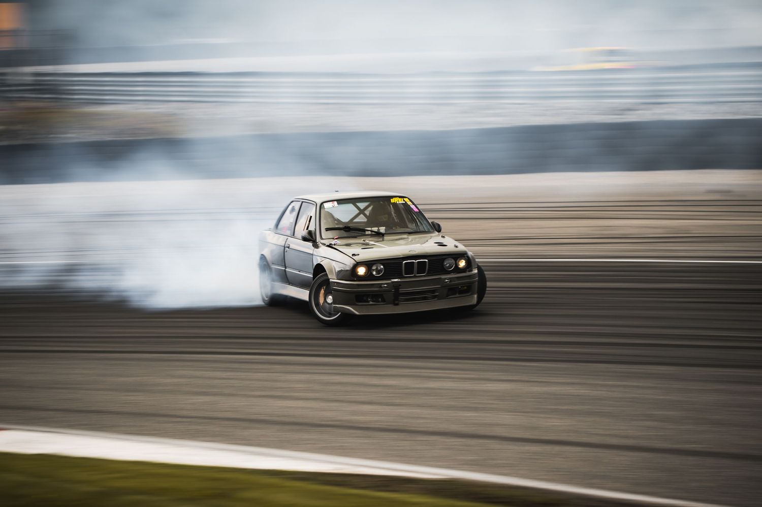 Black BMW E30 M3 drift car creating thick smoke while drifting on motorsport track.