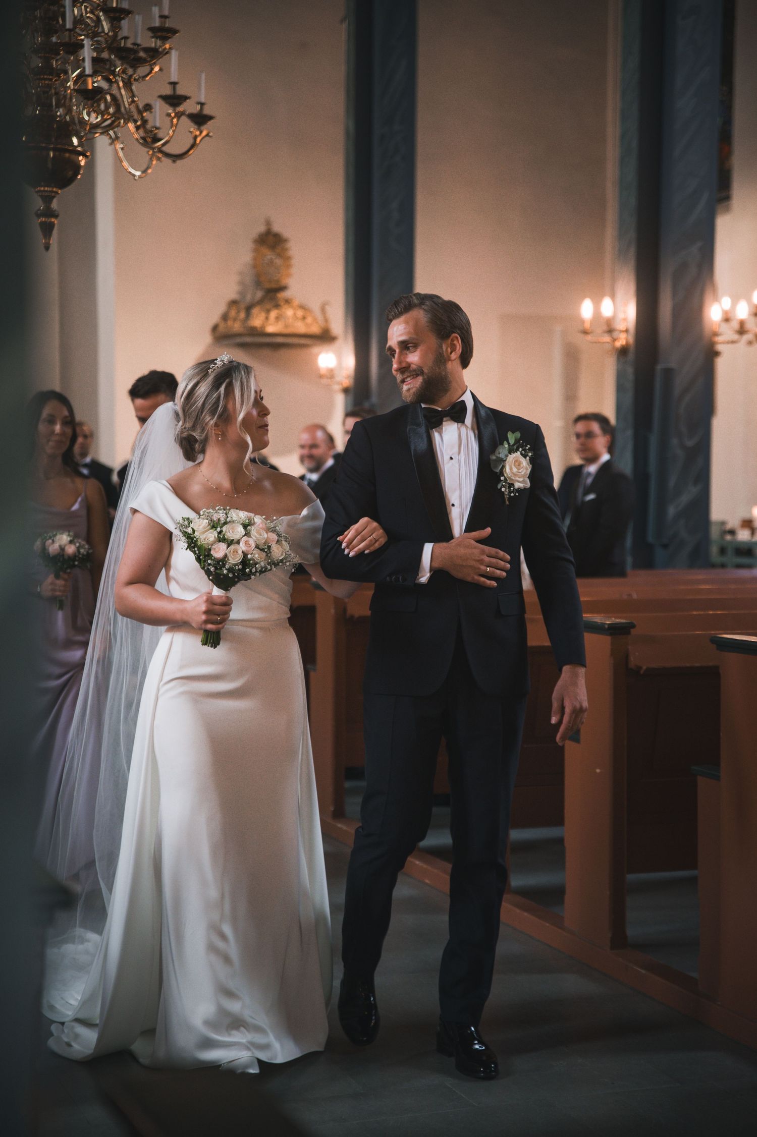 Bride and groom smiling while walking down a candlelit church aisle after ceremony.