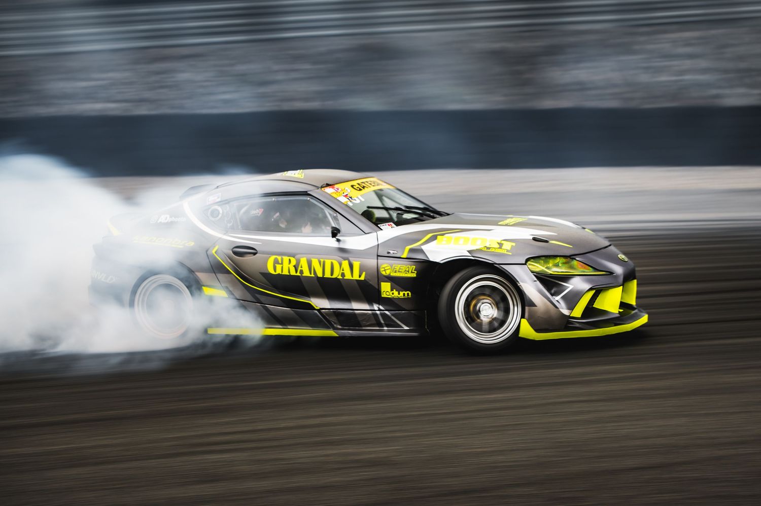 Grandal sponsored yellow drift car performing aggressive drift with heavy smoke on circuit.