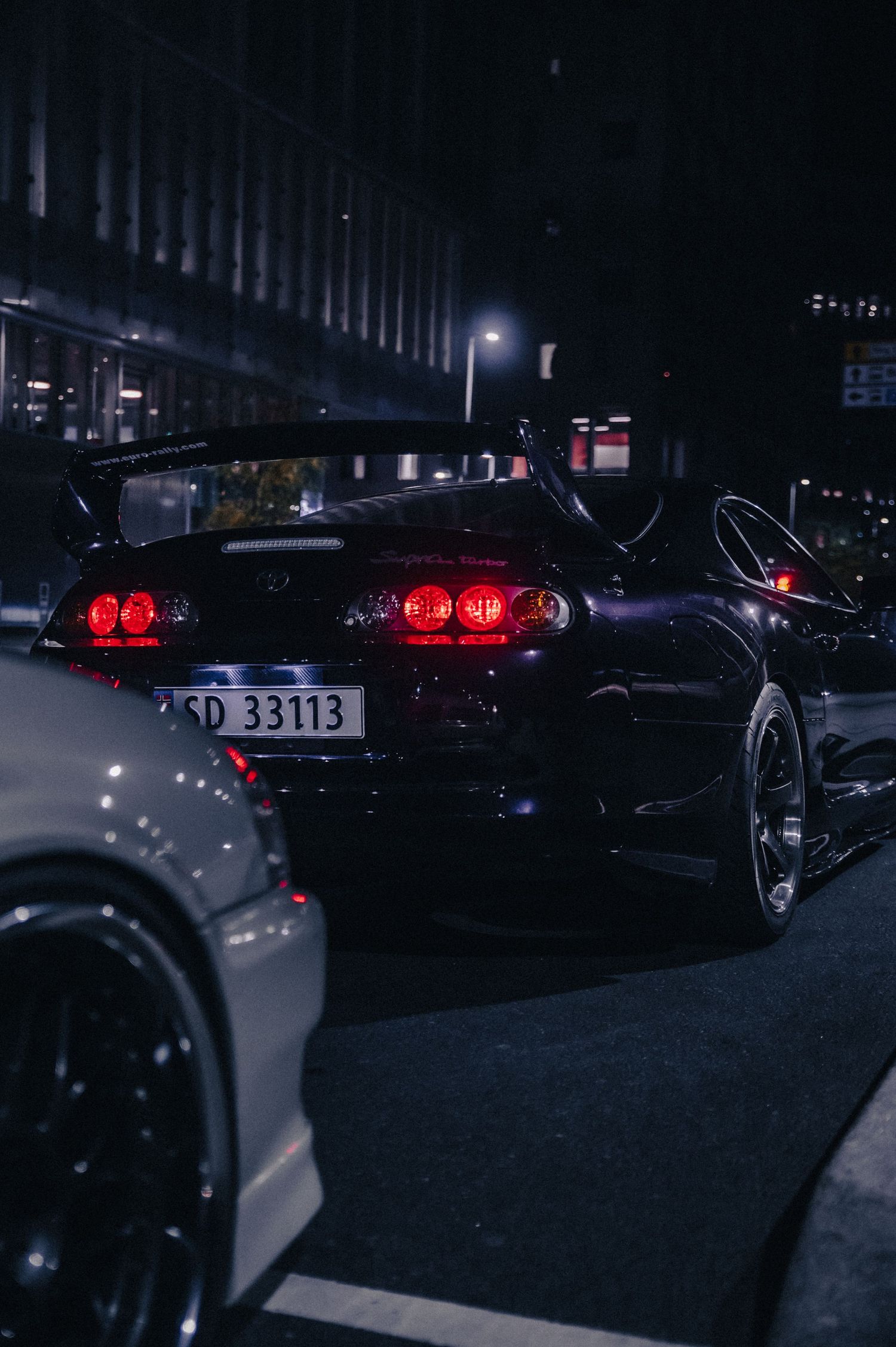 Toyota Supra MK4 with large rear wing parked on a city street at night.